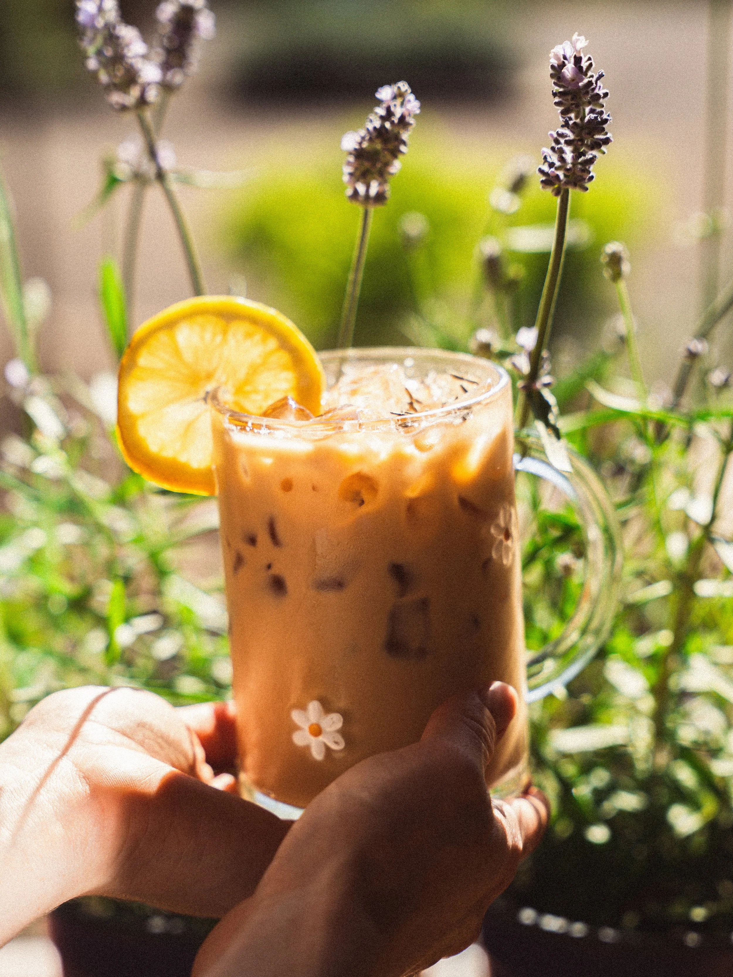 Person holding a glass jar with iced coffee and cream, overflowing with caramel sauce on the outside.