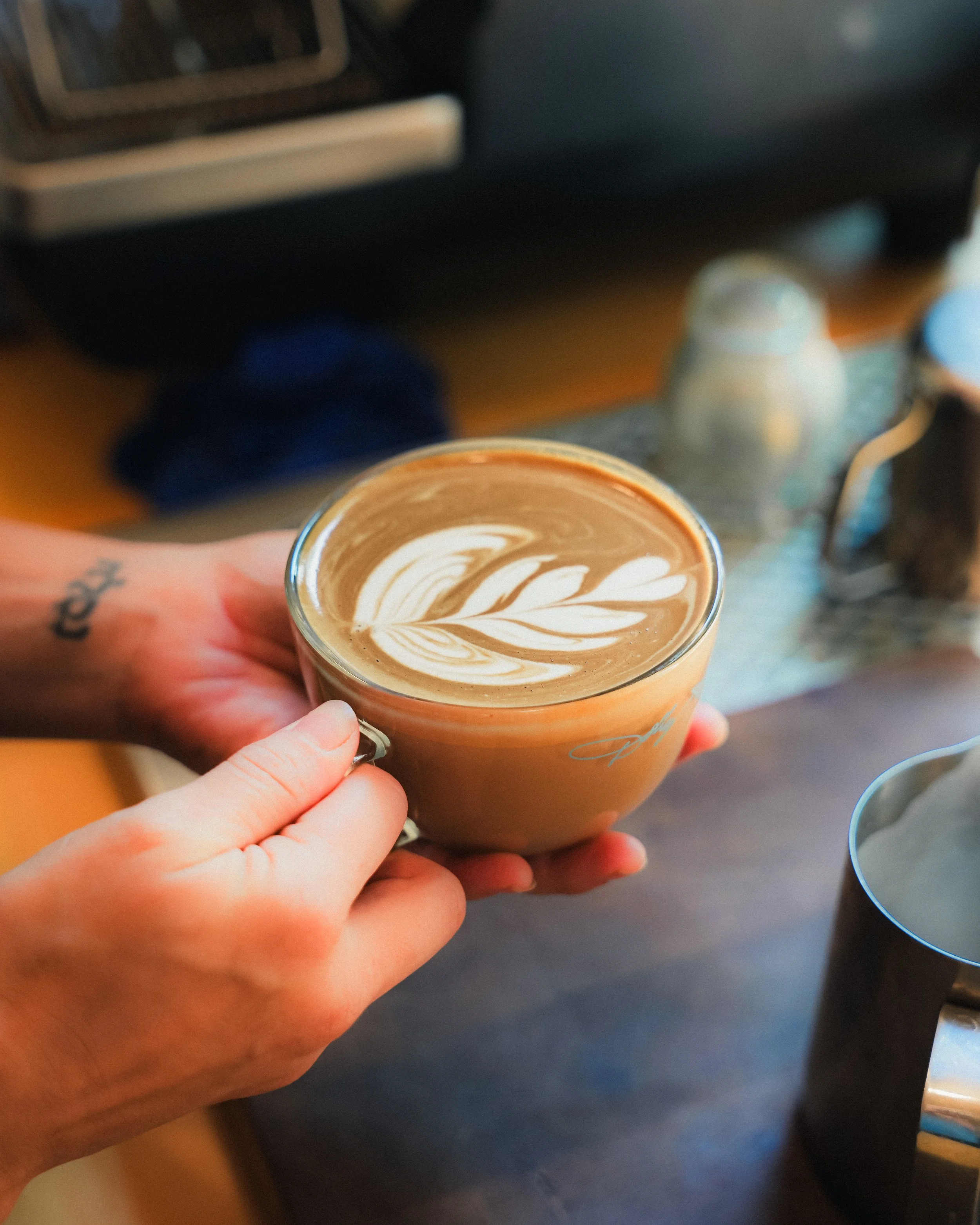 Person holding a glass mug of latte with latte art in a coffee shop.