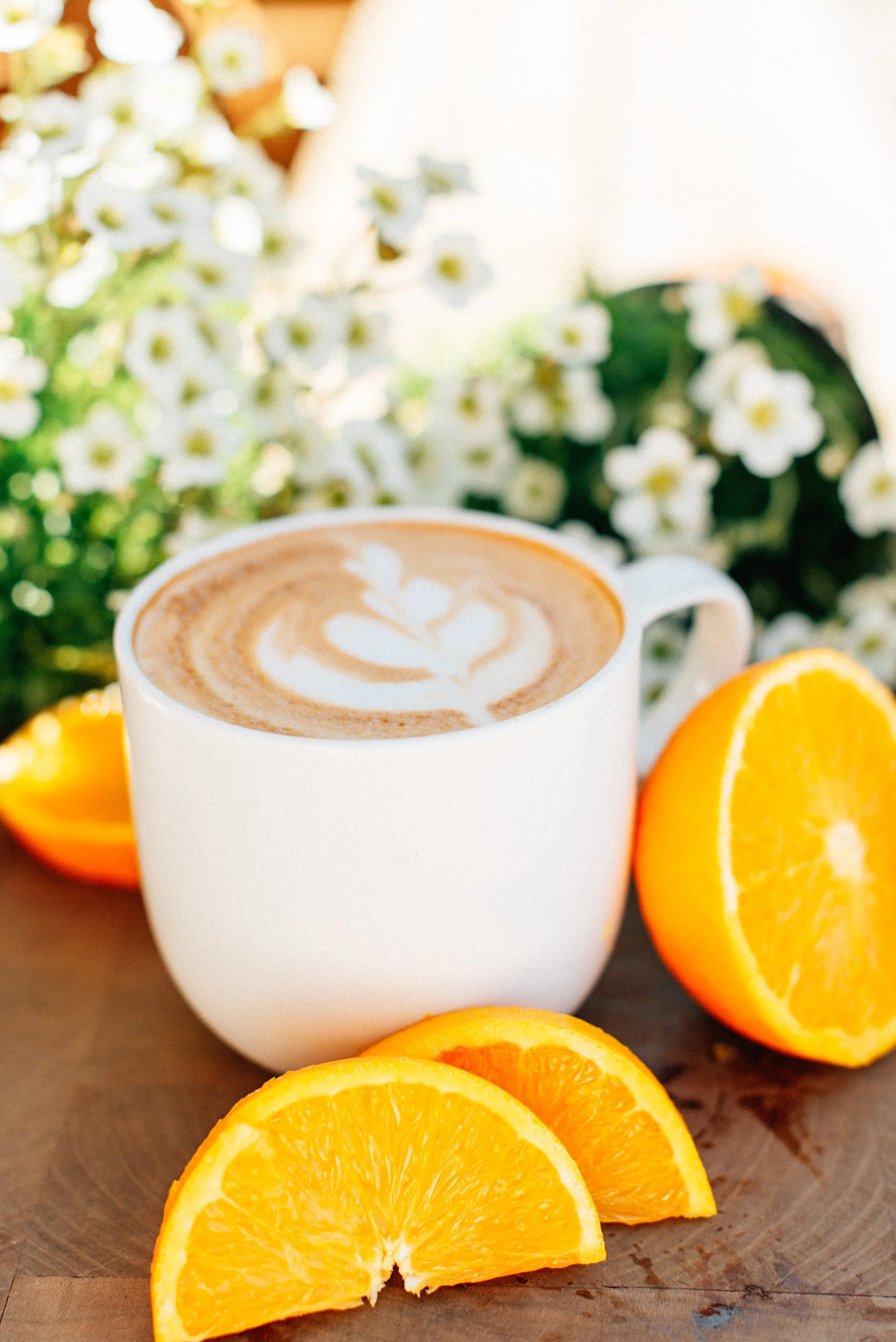A latte with latte art being held above a bed of colorful pink, white, yellow, and purple flowers.