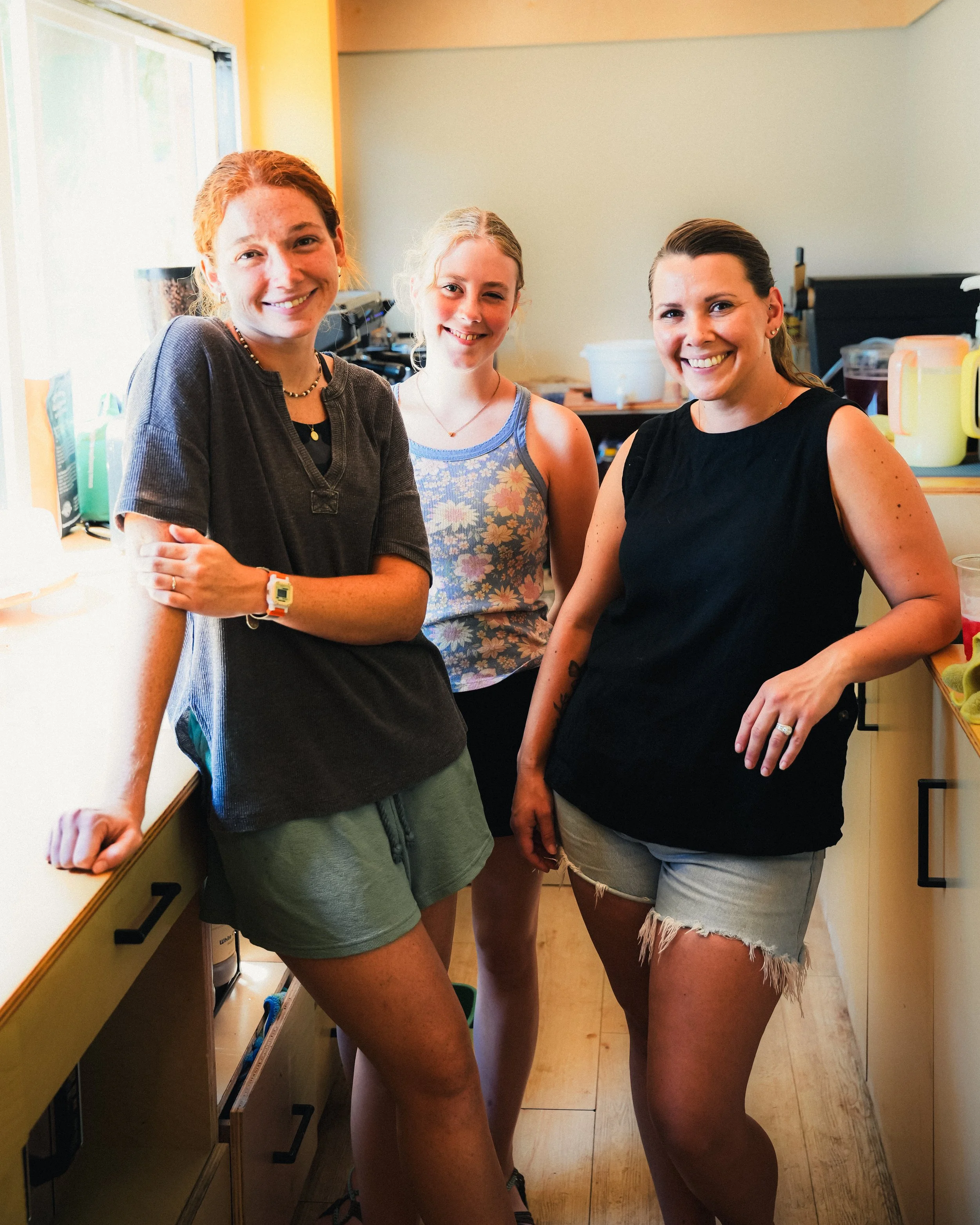 Three women smiling and posing in a kitchen.