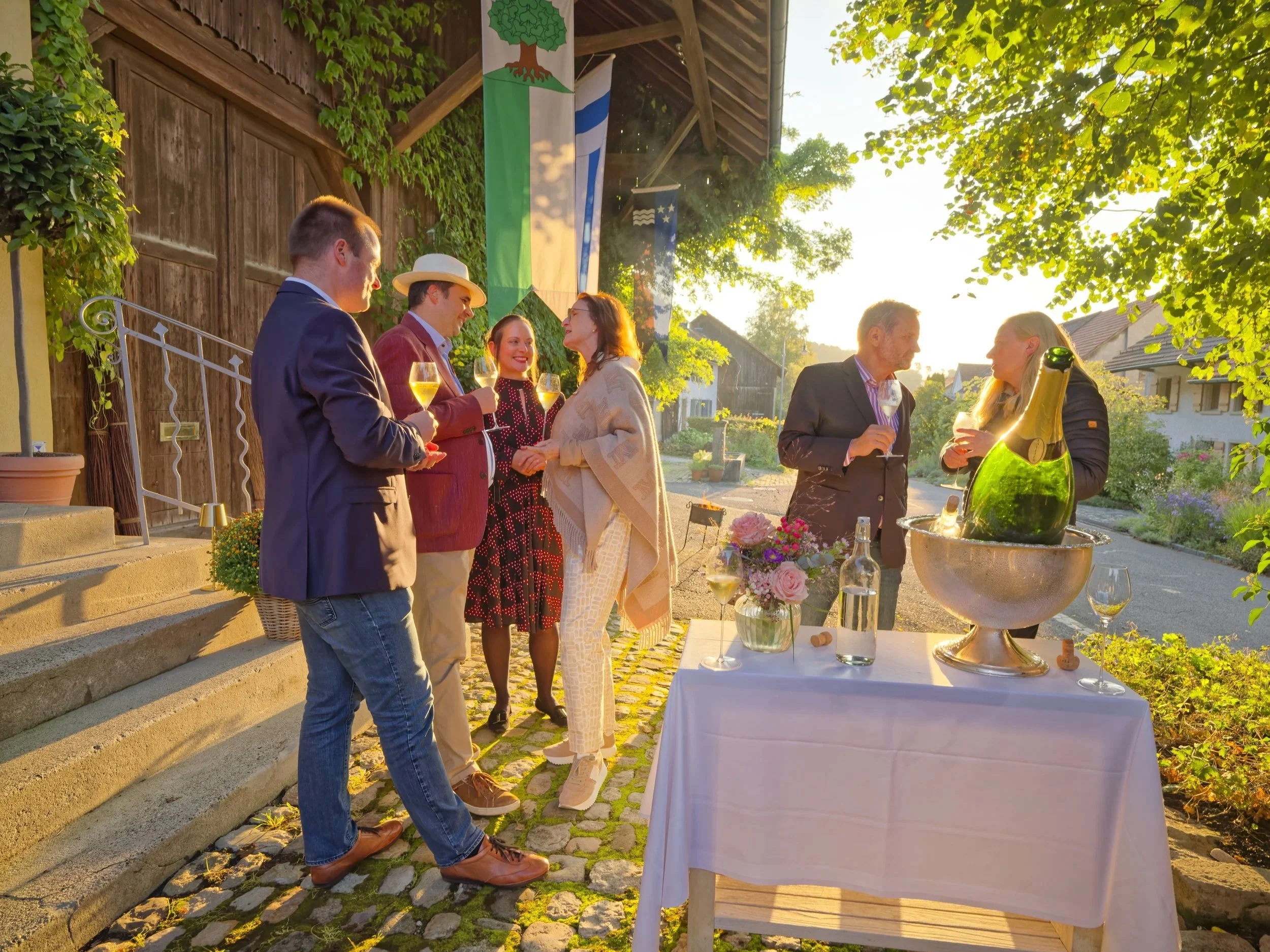 Atmosphärische Aufnahme vom 40 Geburtstag beim Feiern mit Freunden draussen bei Sonnenuntergang, mit Champagner und umgeben von Blumen. 