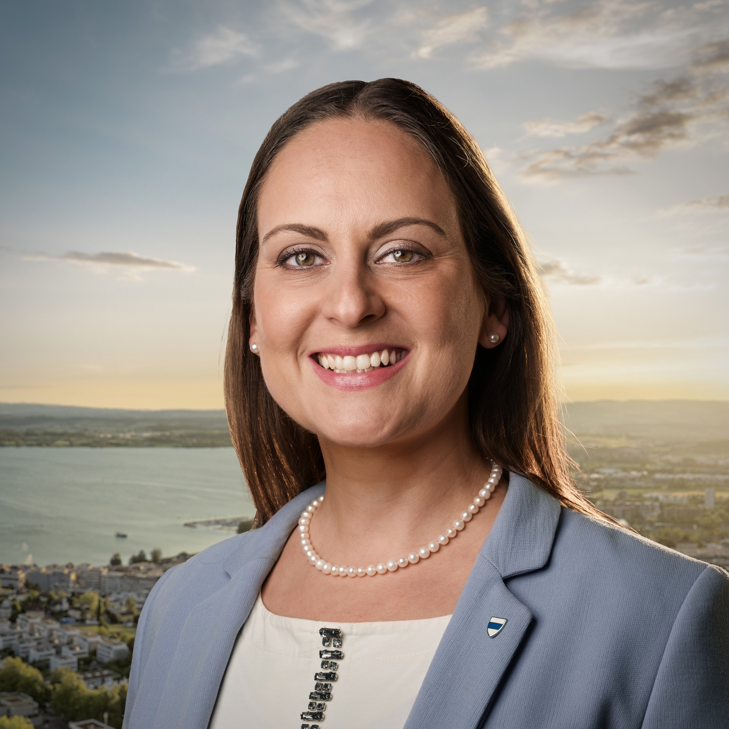 Ein Porträt von Joëlle Gautier vor einer Aufnahme des Kantons Zug mit Blick auf den See bei Sonnenuntergang, die professionell gekleidet ist.