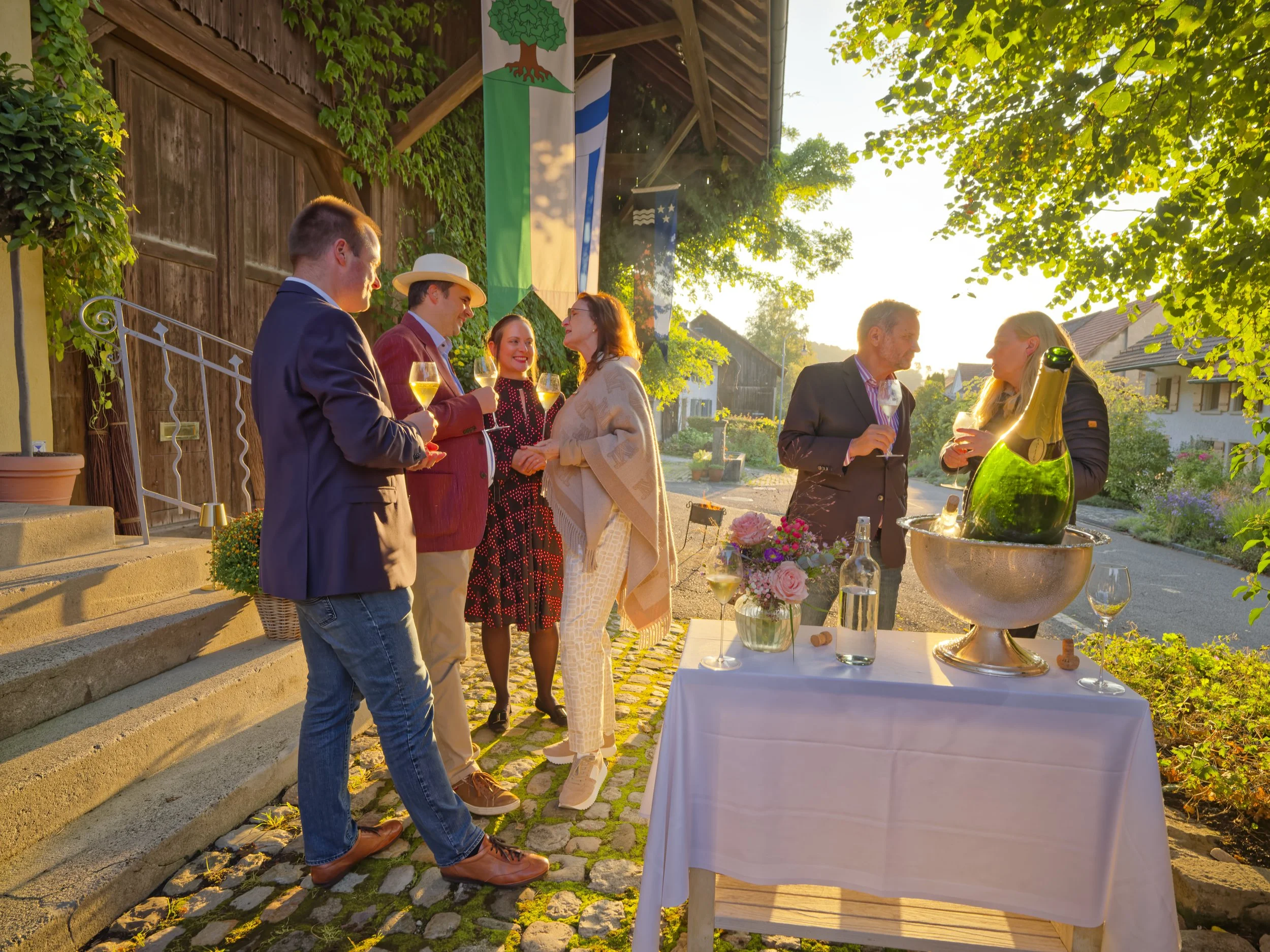Atmosphärische Aufnahme vom 40 Geburtstag beim Feiern mit Freunden draussen bei Sonnenuntergang, mit Champagner und umgeben von Blumen. 