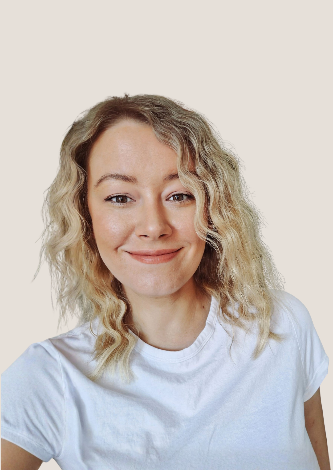 A young woman with blonde, curly hair smiling at the camera, wearing a white T-shirt, against a plain beige background.