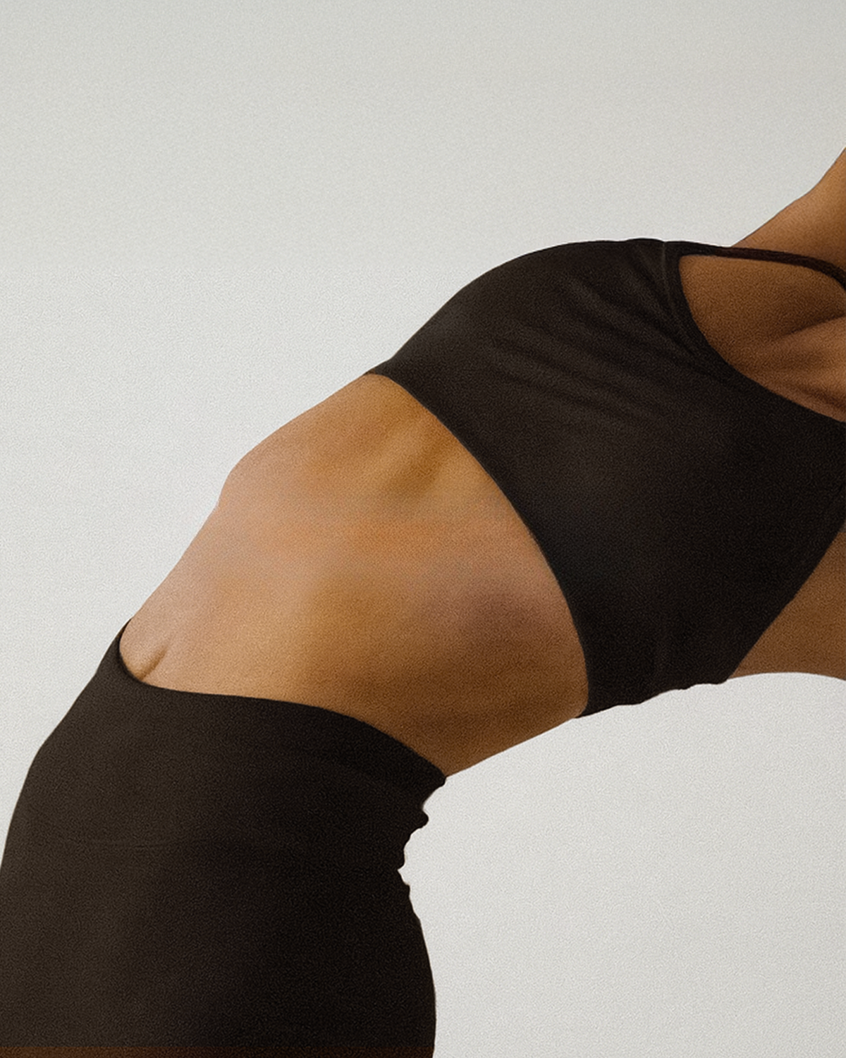 Close-up of a woman's midsection showing her stomach and waist, wearing black athletic clothing.