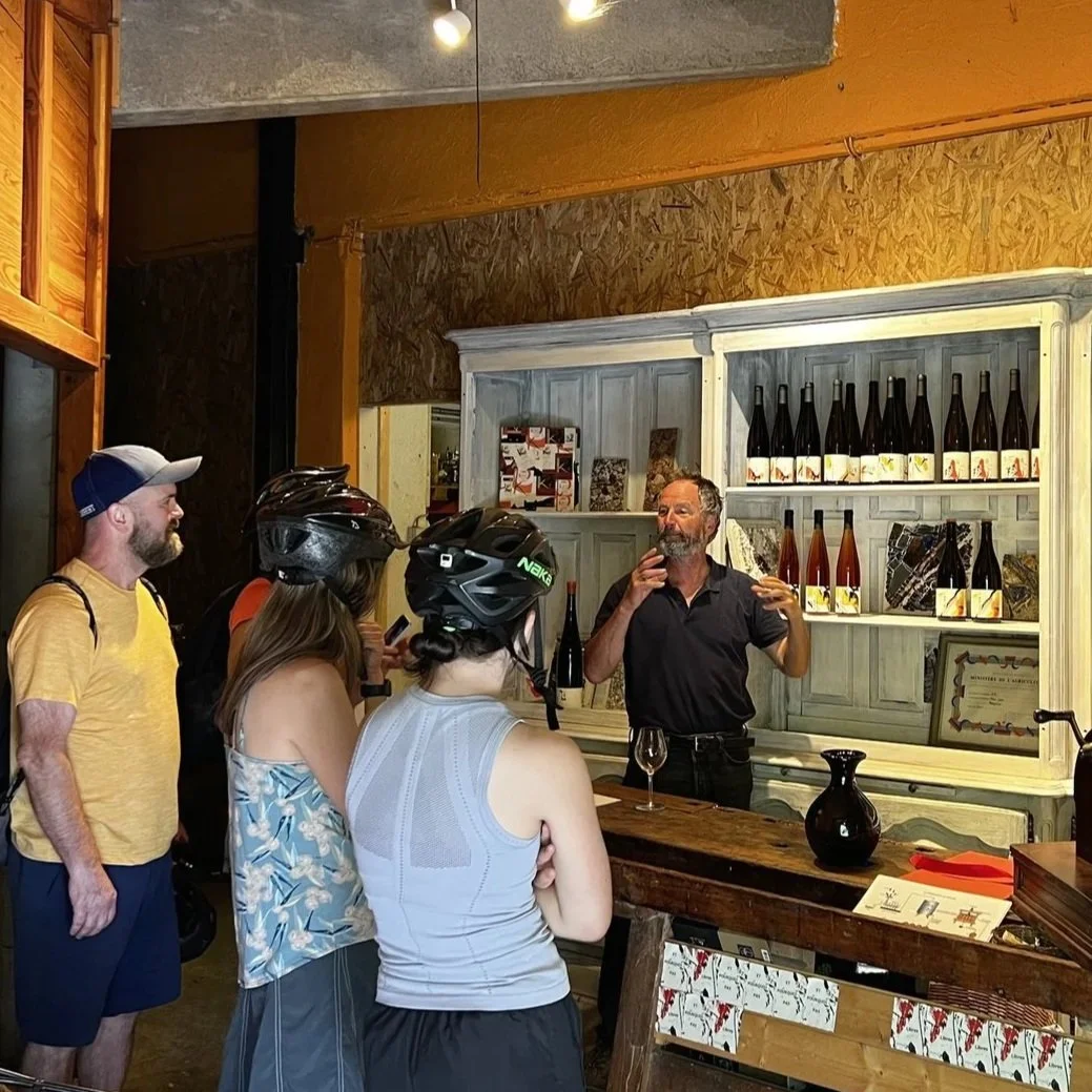 A man is giving a wine tasting at a winery to a group of people inside a rustic wine shop.