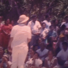 A person facing away, wearing a light-colored hat and shirt, surrounded by a crowd of people outdoors.