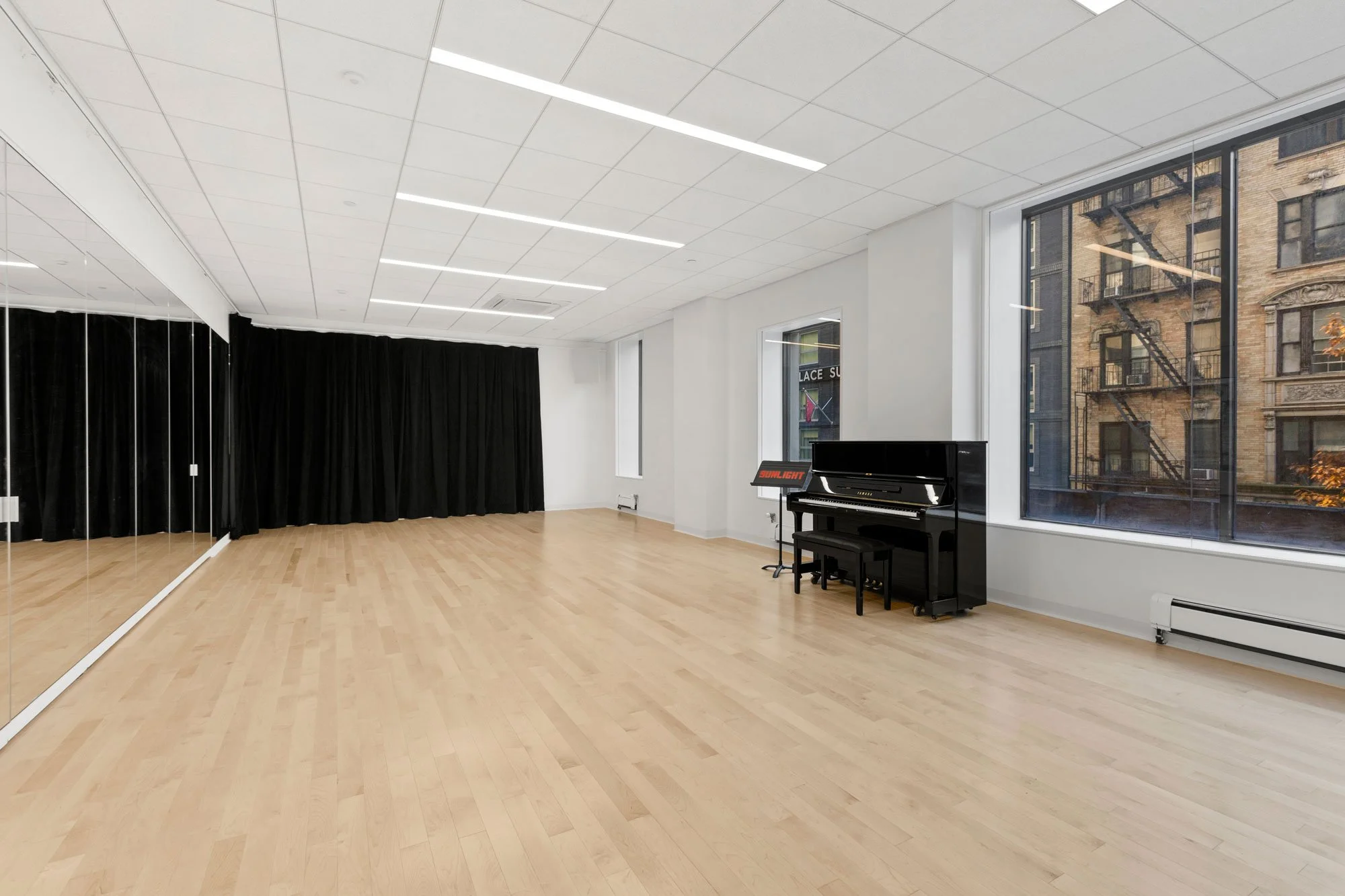 Spacious studio with wood floors, mirrors, curtain and piano
