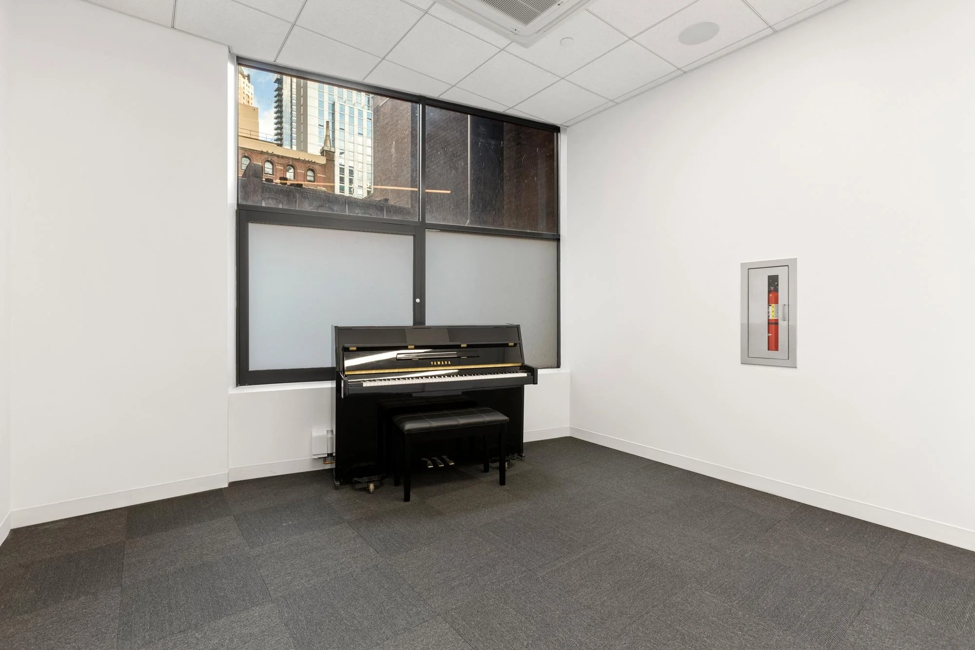 small rehearsal studio with carpet, window and piano
