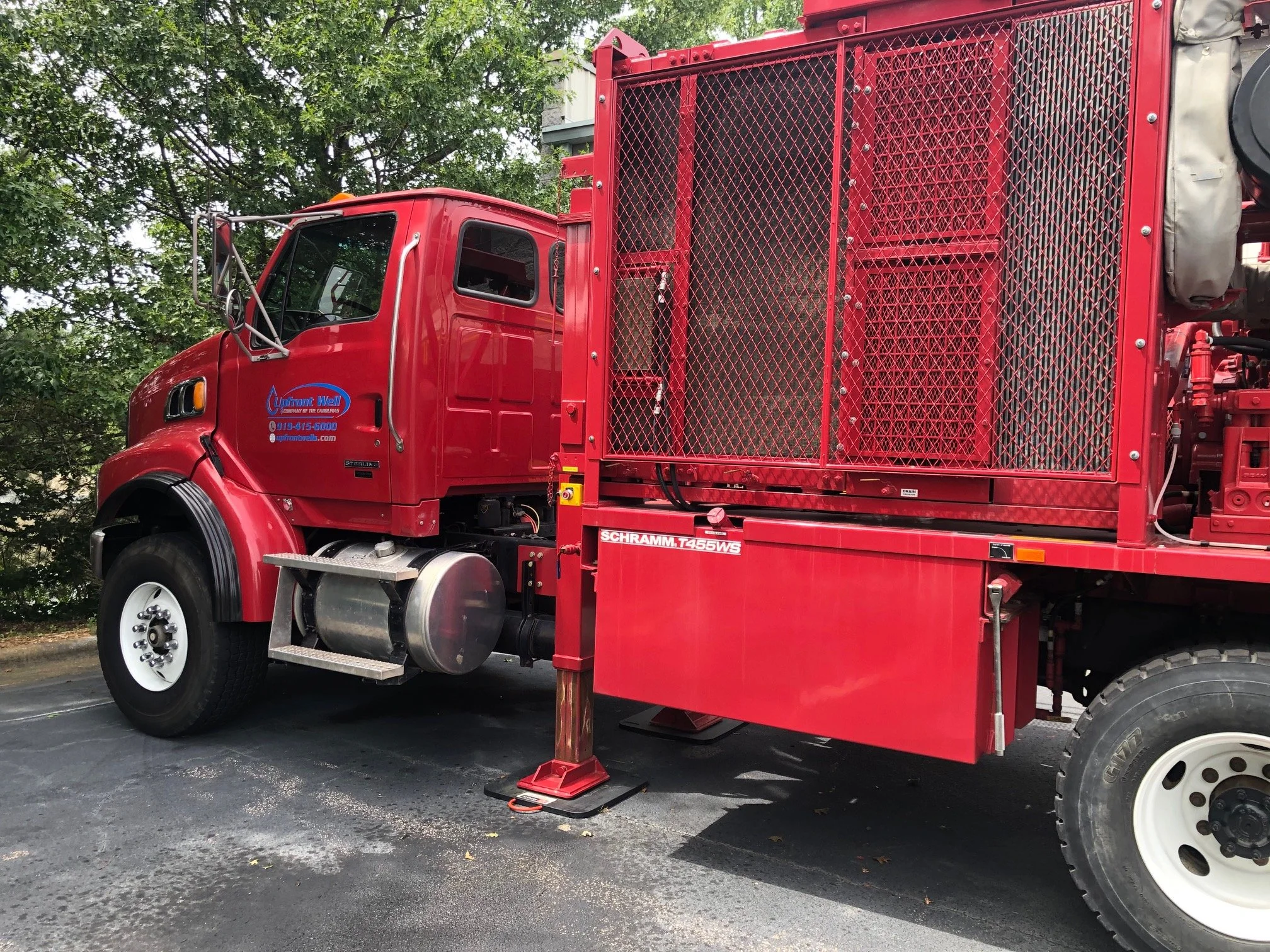 Red firefighting rescue truck parked on asphalt pavement, with metal mesh compartments on side, a large fuel tank under the cab, and trees in the background.