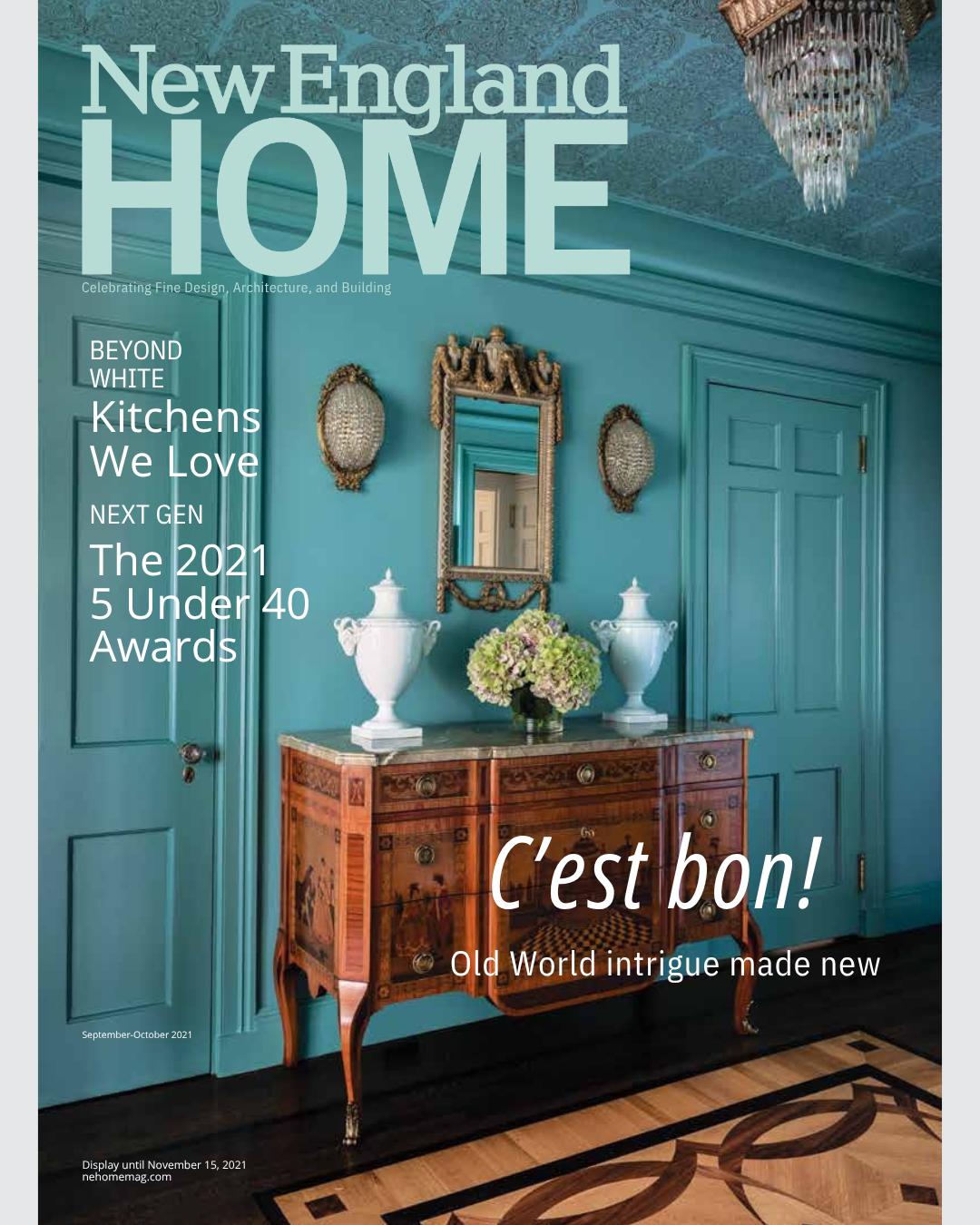 Cover of New England Home magazine featuring a vintage blue wall with a mirror, two wall sconces, and an antique wooden sideboard with a floral arrangement.