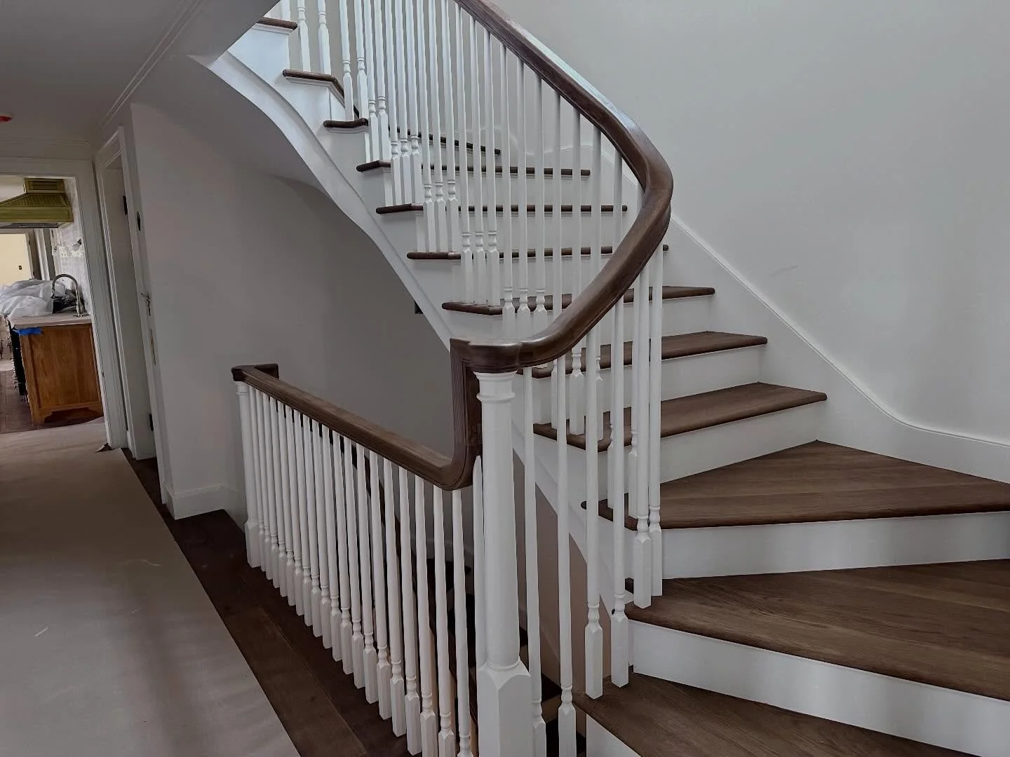 Indoor wooden staircase with white balusters and dark wood handrail, curved design, in a home interior.