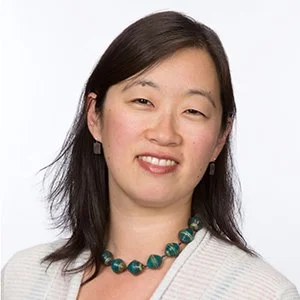 A woman with shoulder-length dark hair smiling against a plain white background.