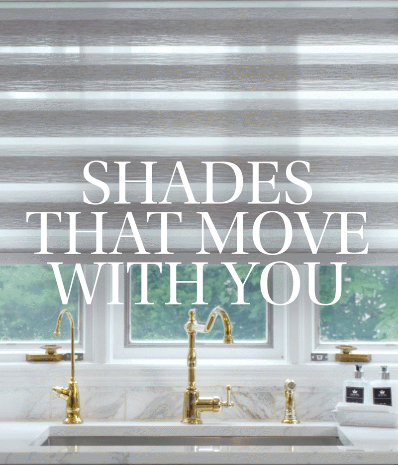 A kitchen window with white shutters and gold faucets over a marble countertop with soap dispensers, greenery visible outside.