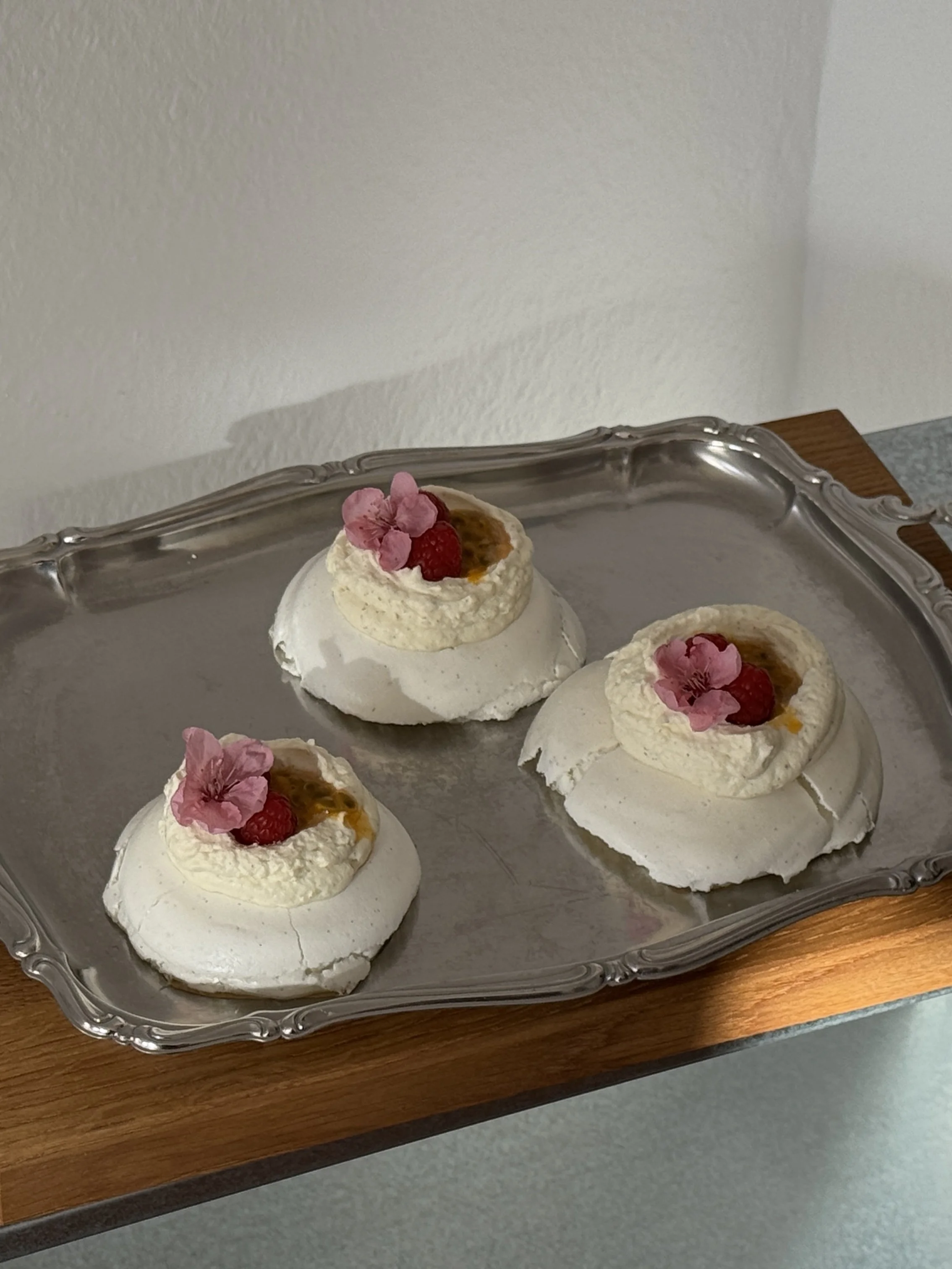 Three small lemon pies with whipped topping, strawberries, raspberries, and pink edible flowers on a silver tray.