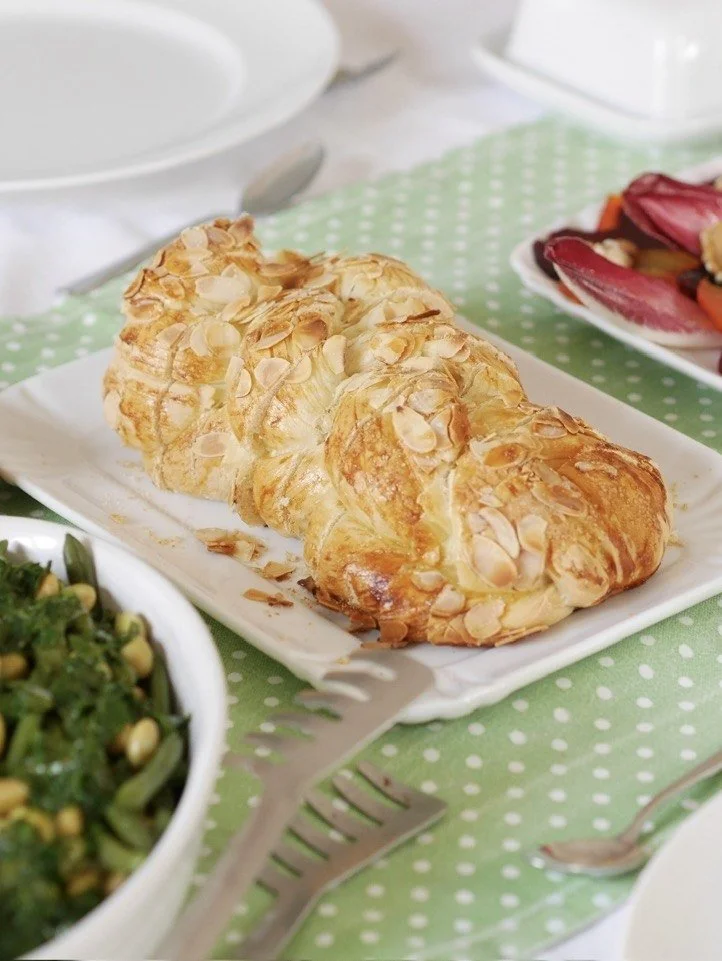 Almond croissant on a white plate on green polka dot tablecloth, with salad and other dishes visible.