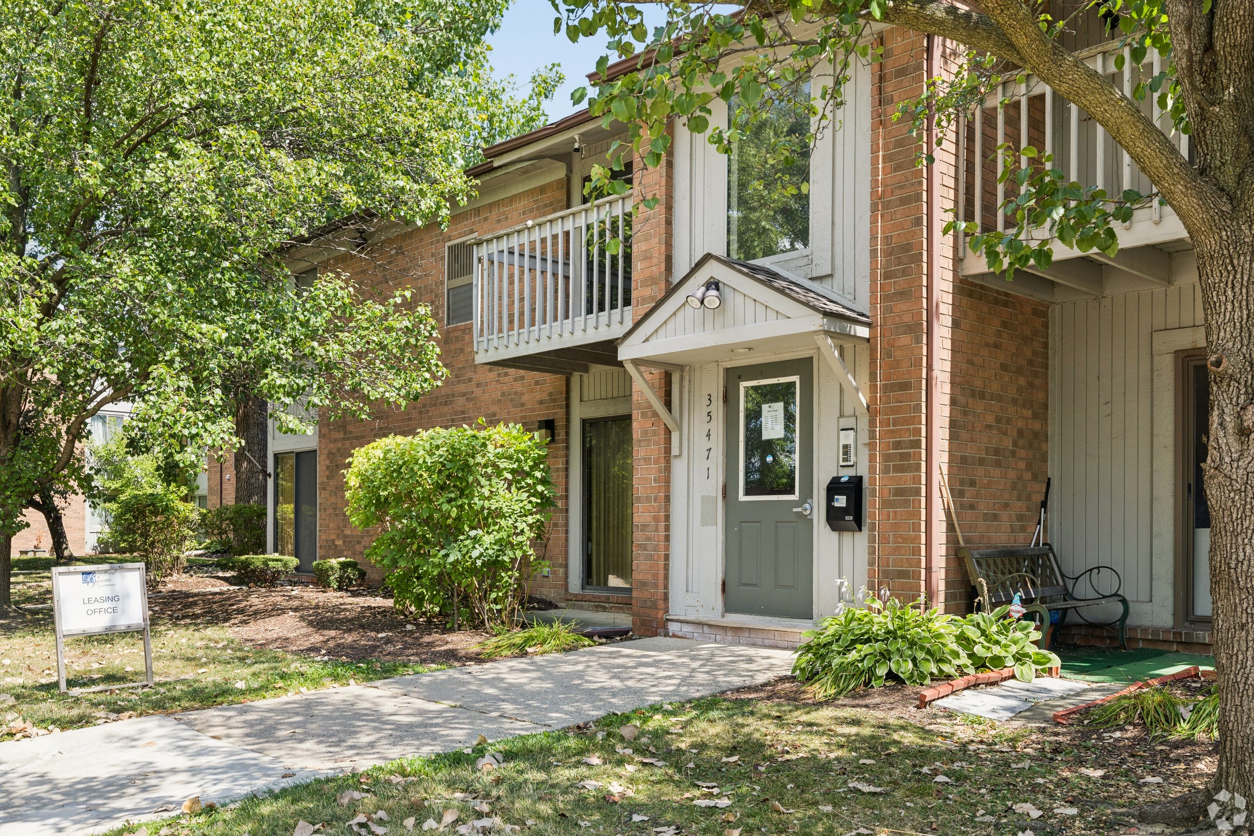 Two-story residential building with balconies, brick and siding exterior, located at 35471, with a small front yard, shrubs, and a sign indicating it is a leasing office.