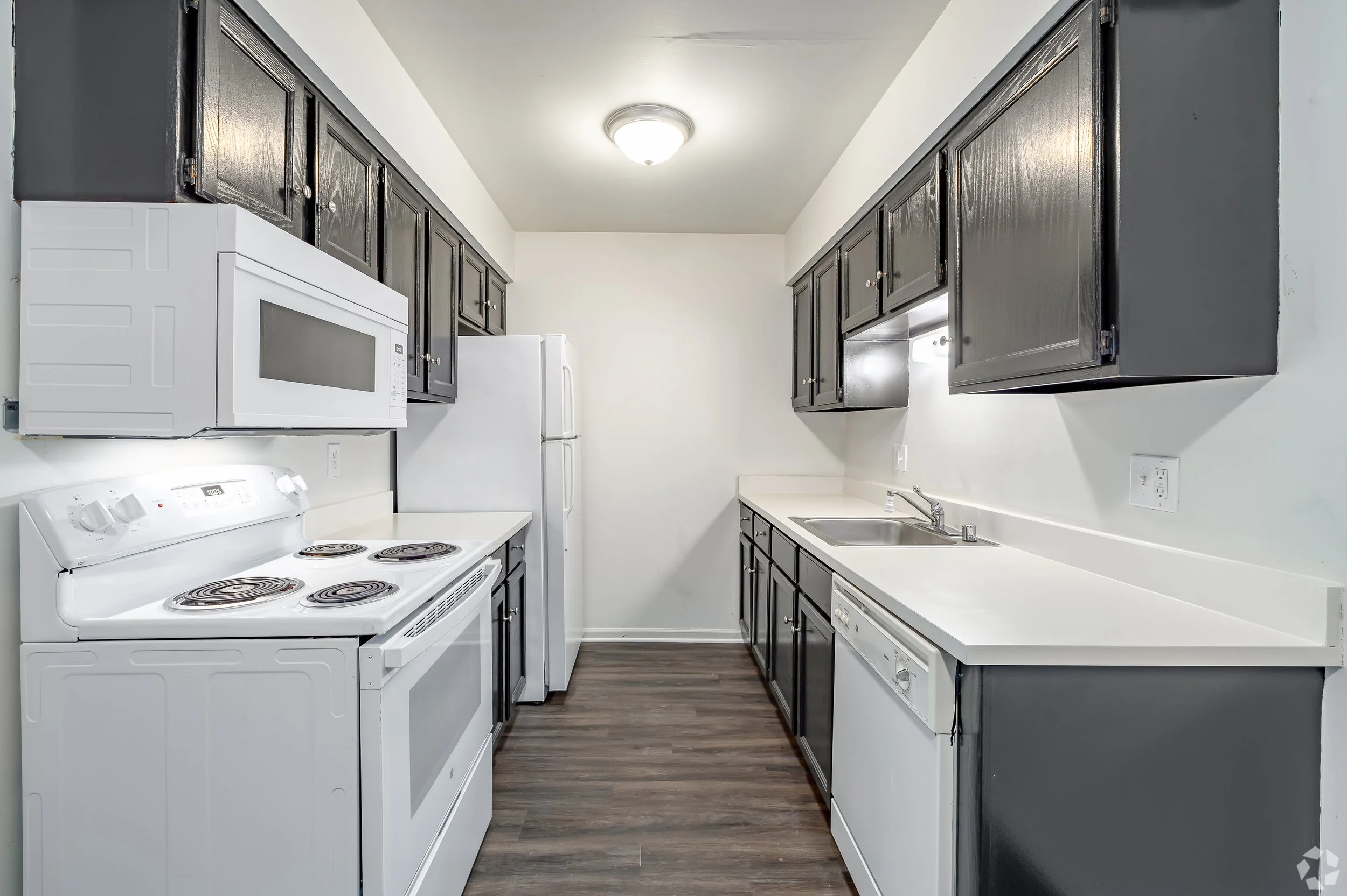 Kitchen with white appliances, dark upper cabinets, and light countertops.