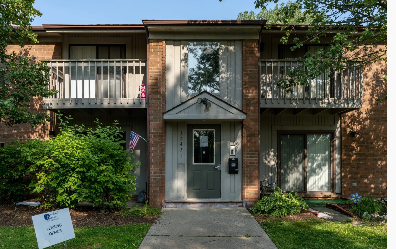 Two-story residential building with balconies, brick and siding exterior, located at 35471, with a small front yard, shrubs, and a sign indicating it is a leasing office.
