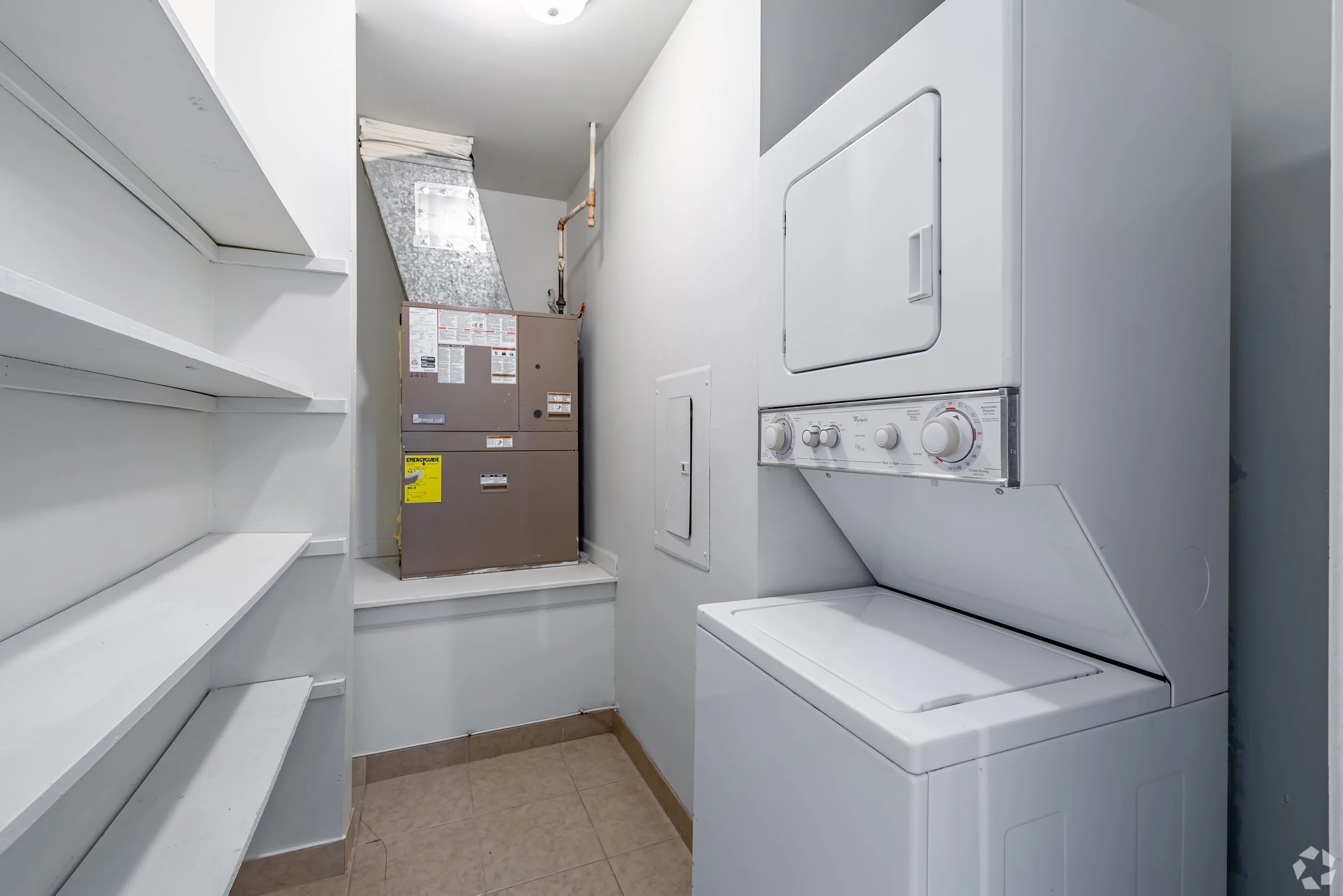 Small laundry room with a stacked washer and dryer, utility shelves on the left, and an HVAC unit on the back wall.