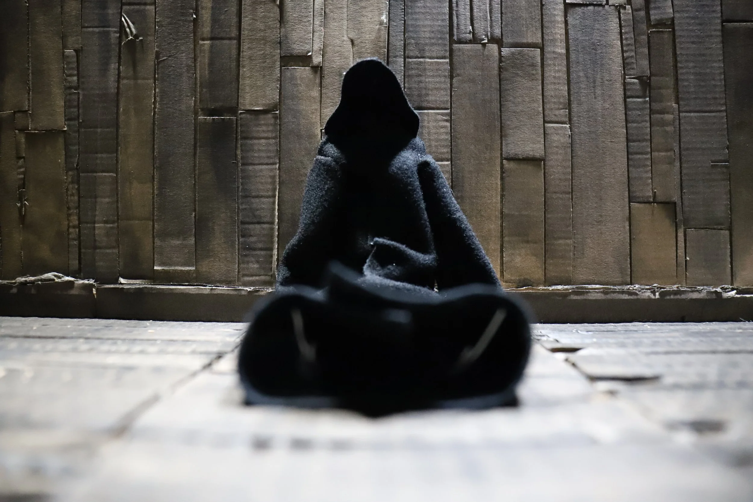 Una persona seduta con le gambe distese davanti, vista di schiena, contro una parete di legno.