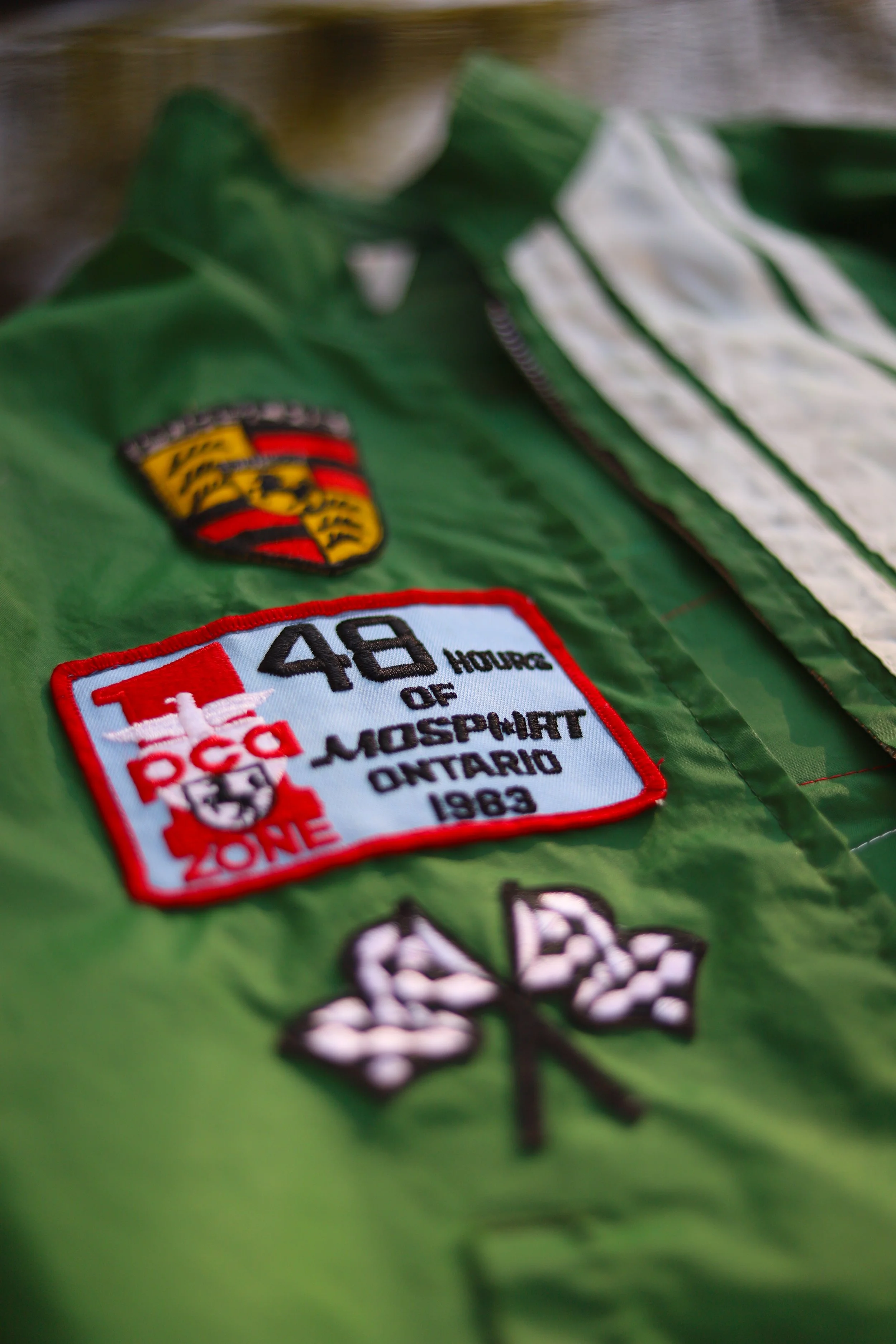 Ricamo e patch su una giacca verde, con il logo di Porsche, un'etichetta che ricorda 48 ore di Monster Ontario 1983 e un simbolo di foglie