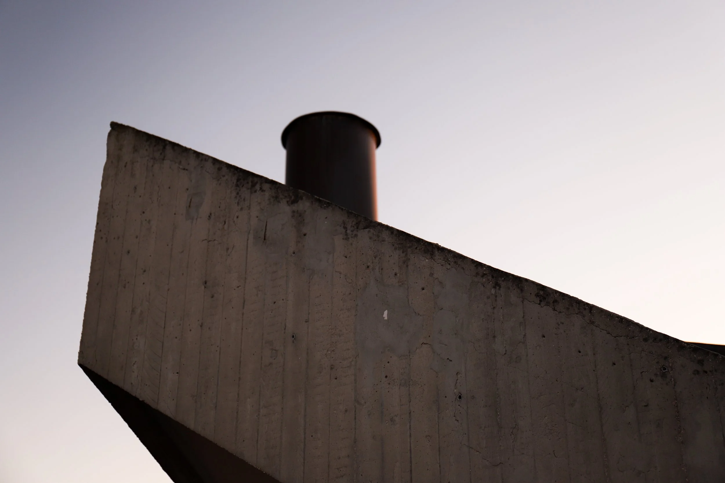 Particolare di un muro di cemento con tubature in alto, sotto un cielo senza nuvole.