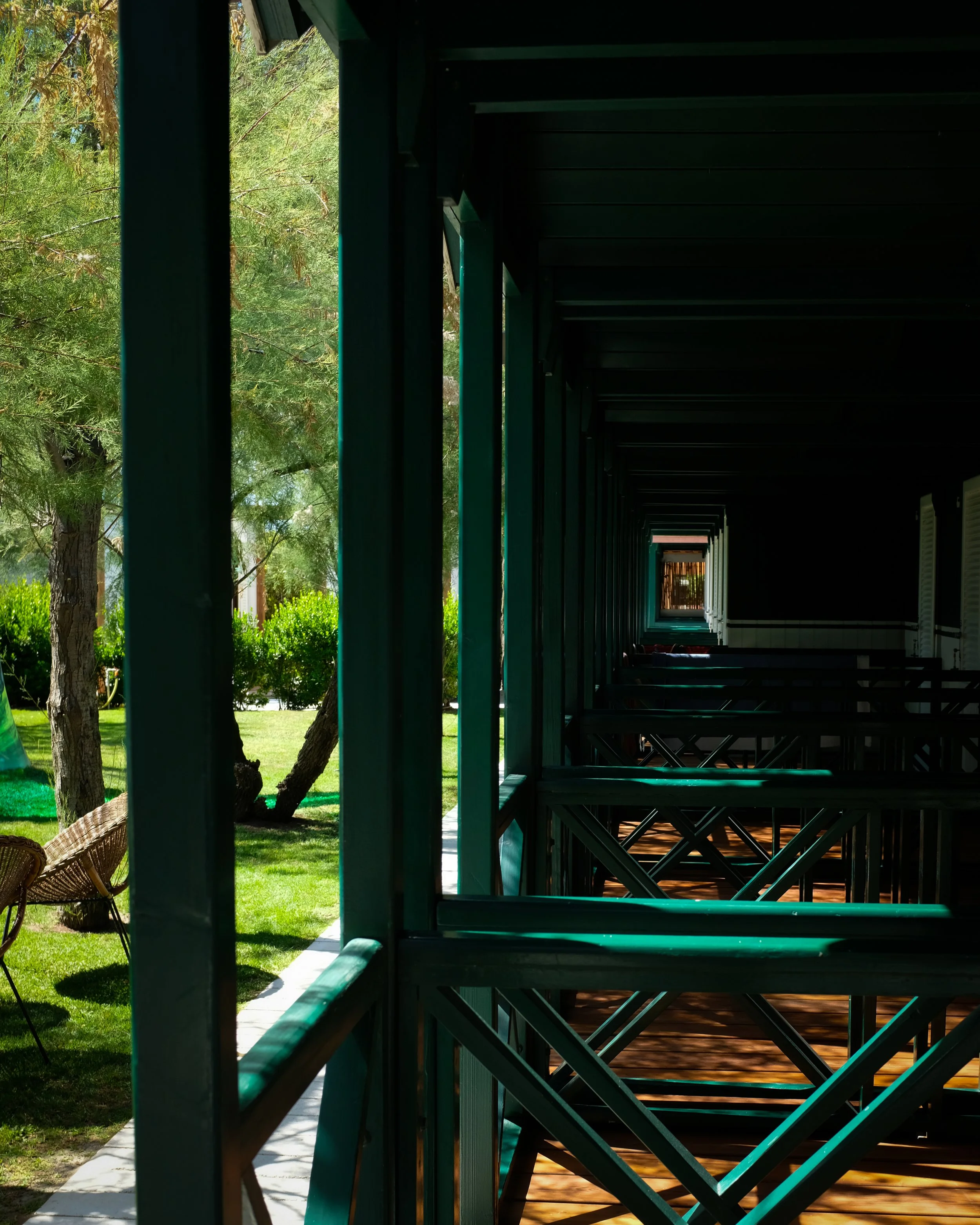 Balcone di uno stabile con ringhiere verdi e sedie di vimini, vista sul giardino con alberi e cespugli