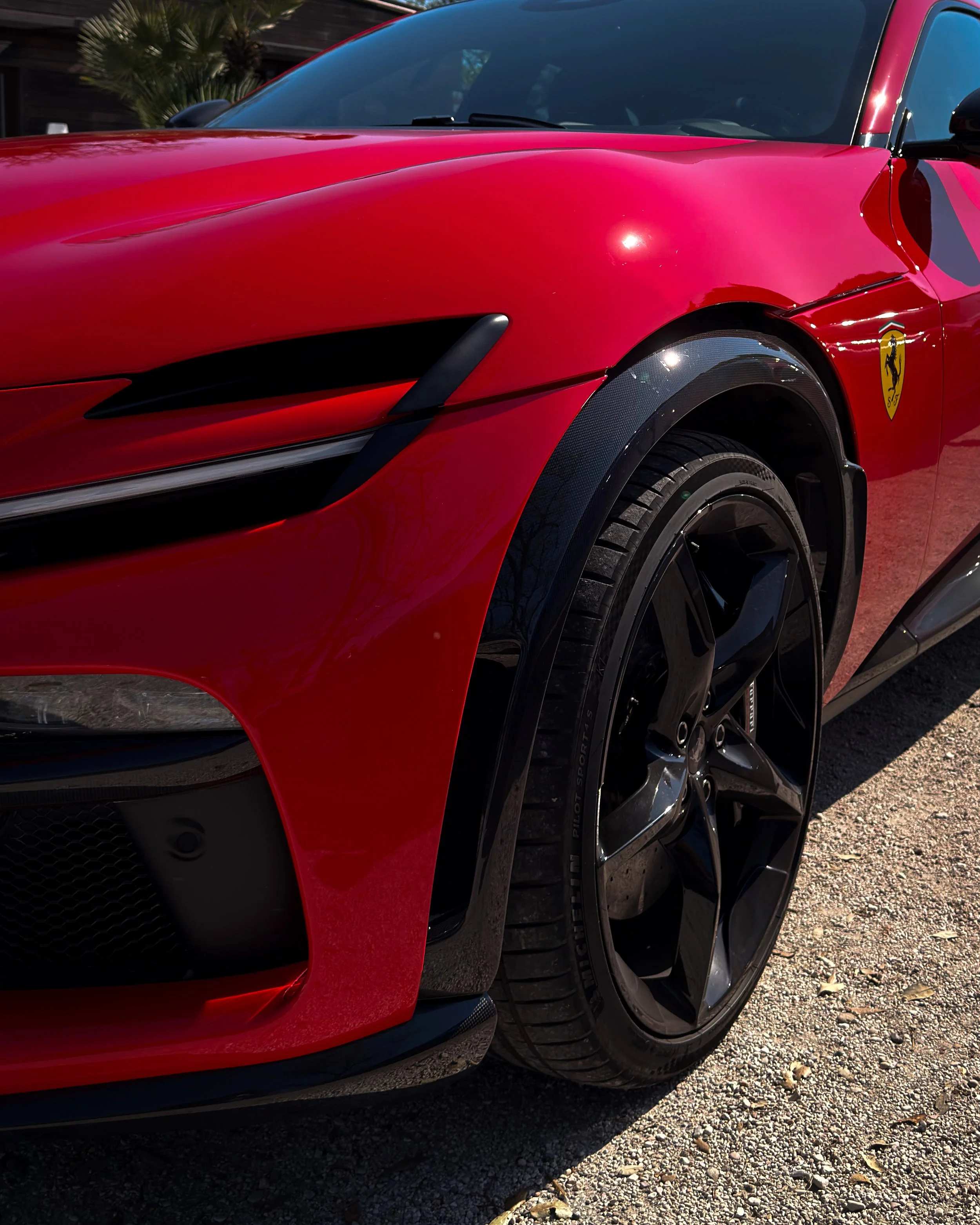 Dettaglio di una Ferrari rossa con logo sul fianco, evidenziando parte del muso e l'anteriore della vettura