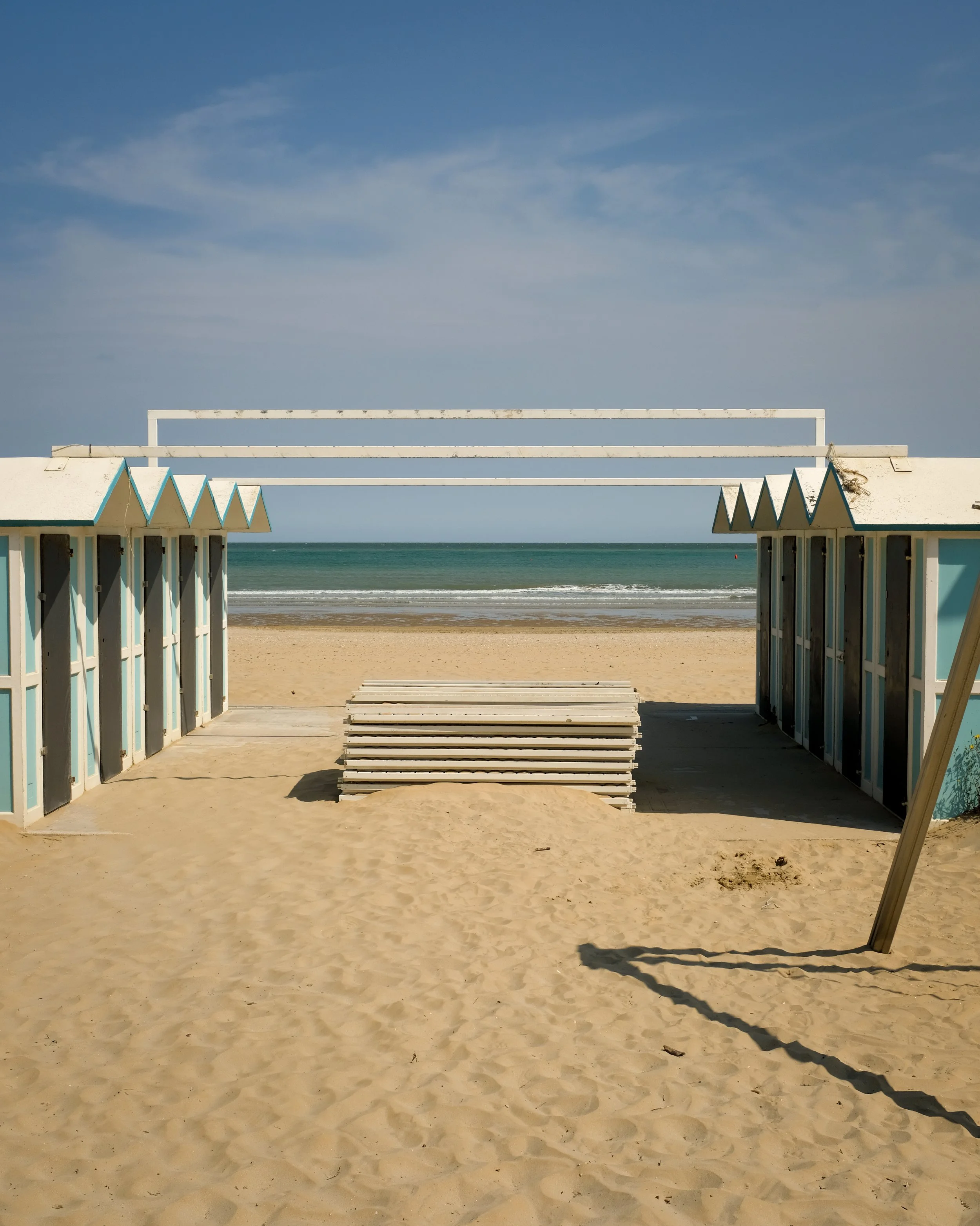 Passeggiata sulla spiaggia con cabine e sedie a sdraio vuote, vista sull'oceano e cielo sereno.