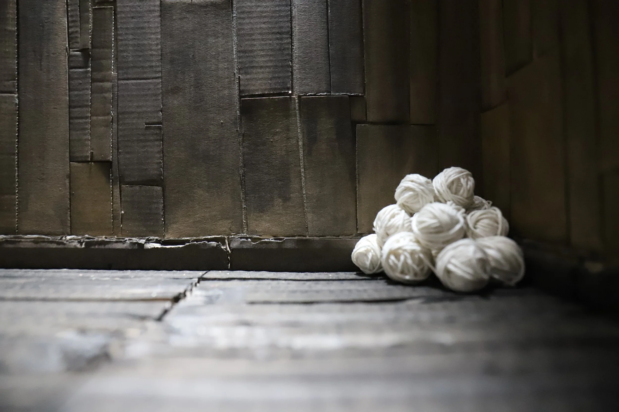 Un mucchio di palline di cotone bianche posizionato in un angolo sul pavimento in legno, con uno sfondo di parete in legno.