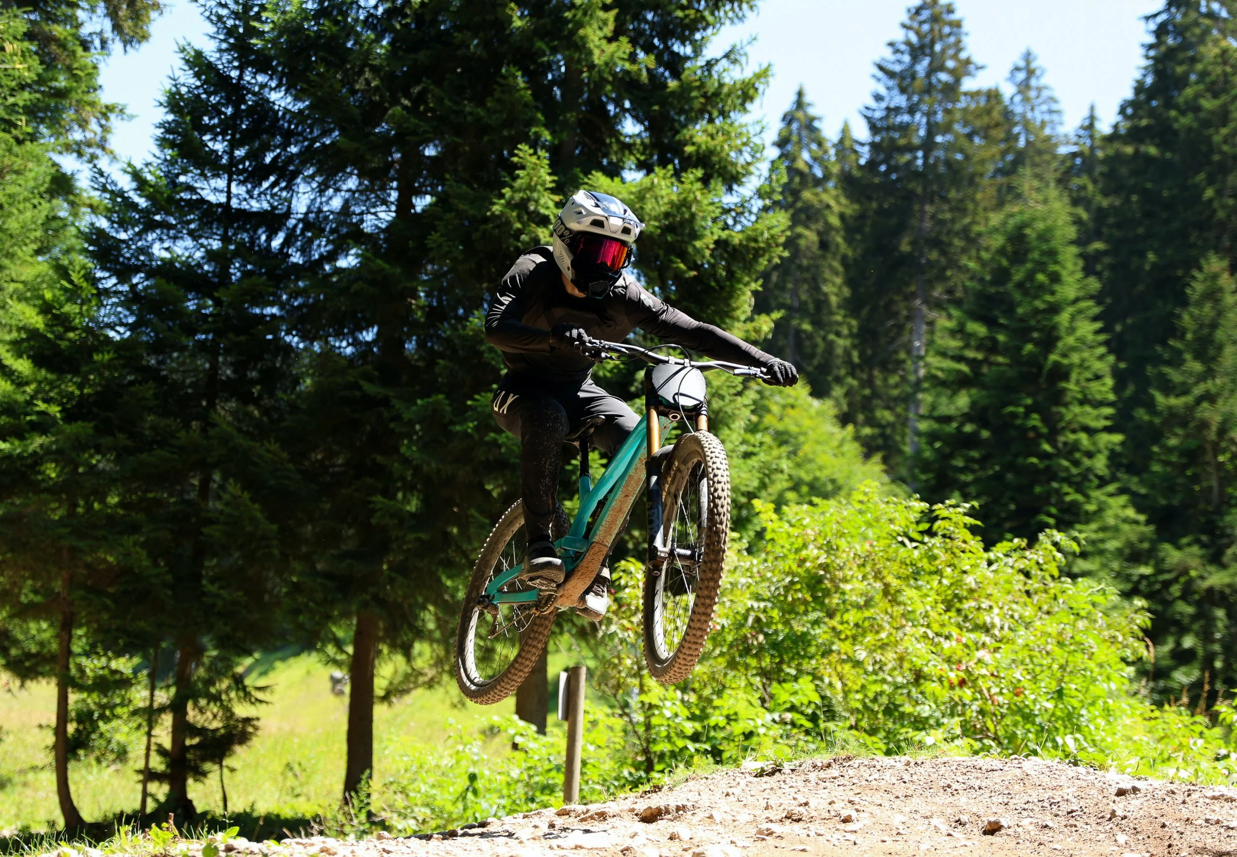 Giocatore di downhill in bici che salta un ostacolo nel bosco.