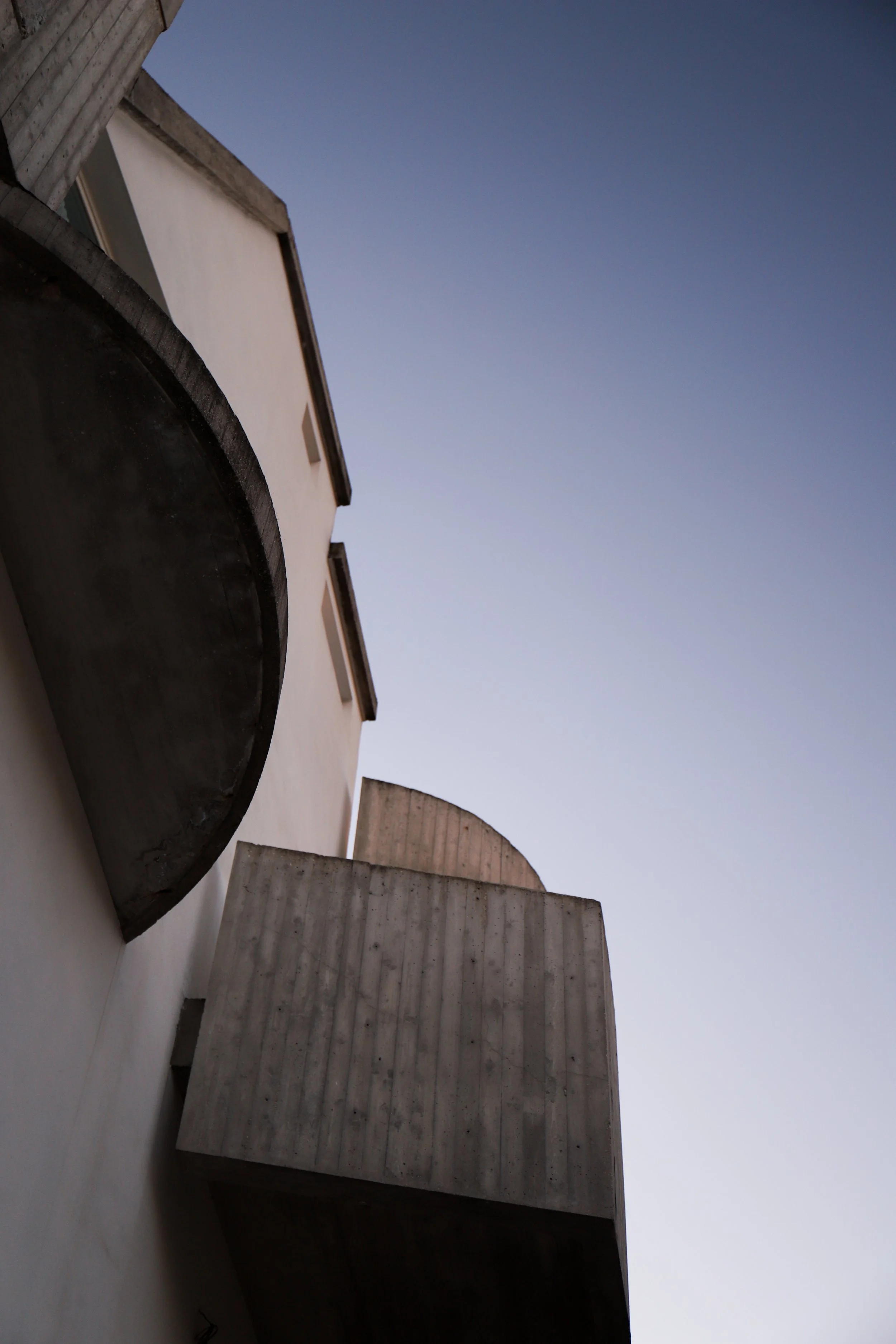 Vista di un edificio moderno con balconi in cemento e pareti bianche, sotto un cielo chiaro e privo di nuvole.