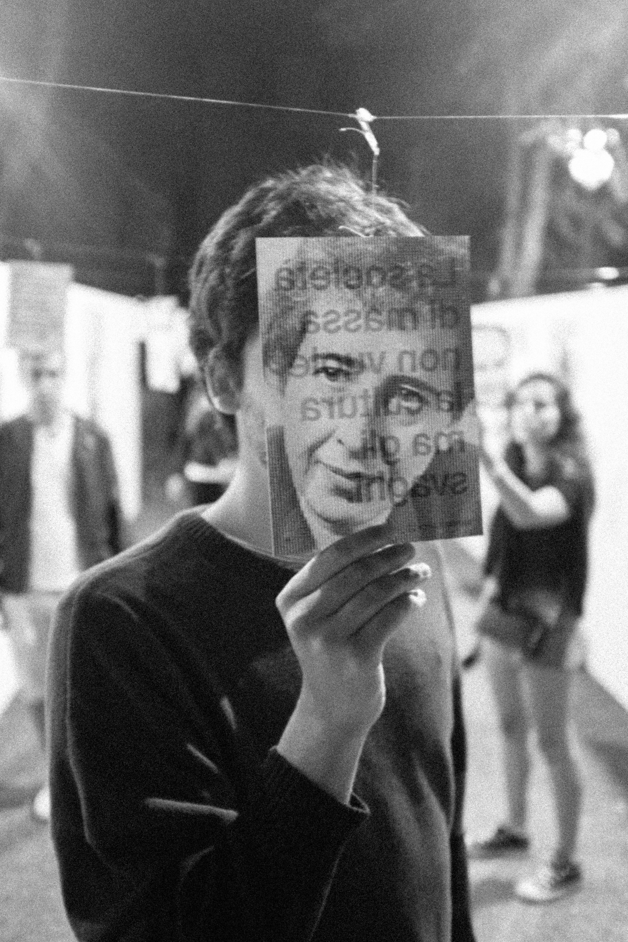 Persona che tiene un opuscolo con il volto di una donna davanti al volto, in bianco e nero.