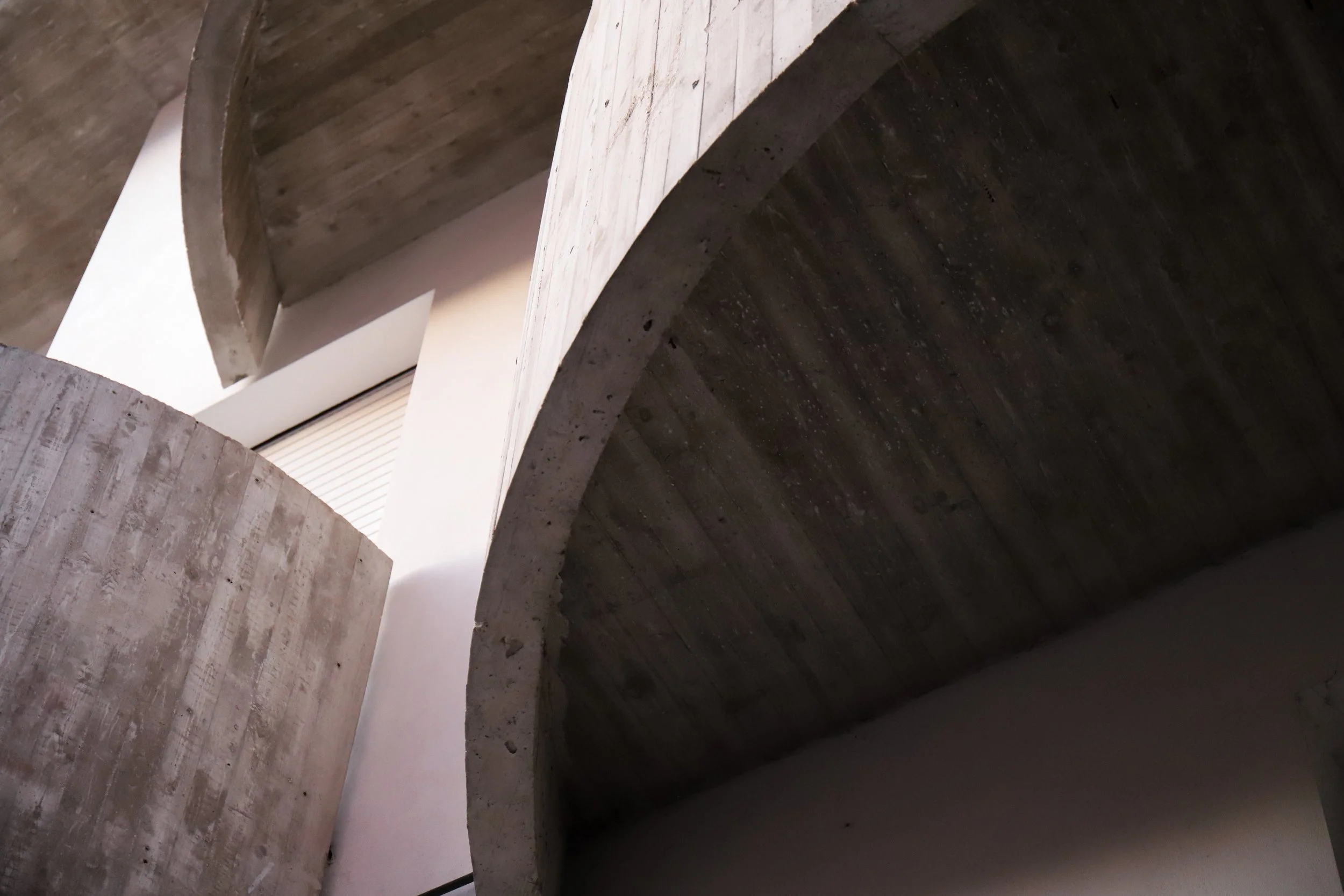 Struttura architettonica con superfici in cemento e legno, veduta dal basso che evidenzia archi e curve.