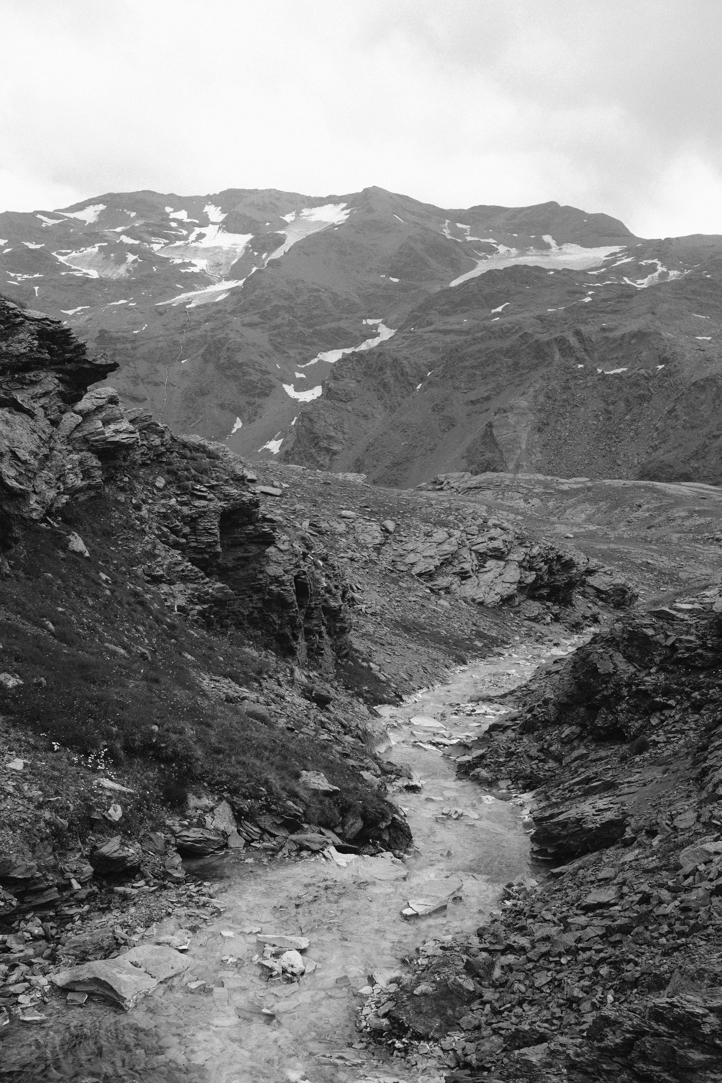 Paesaggio montano con rocce e un piccolo ruscello, in bianco e nero.