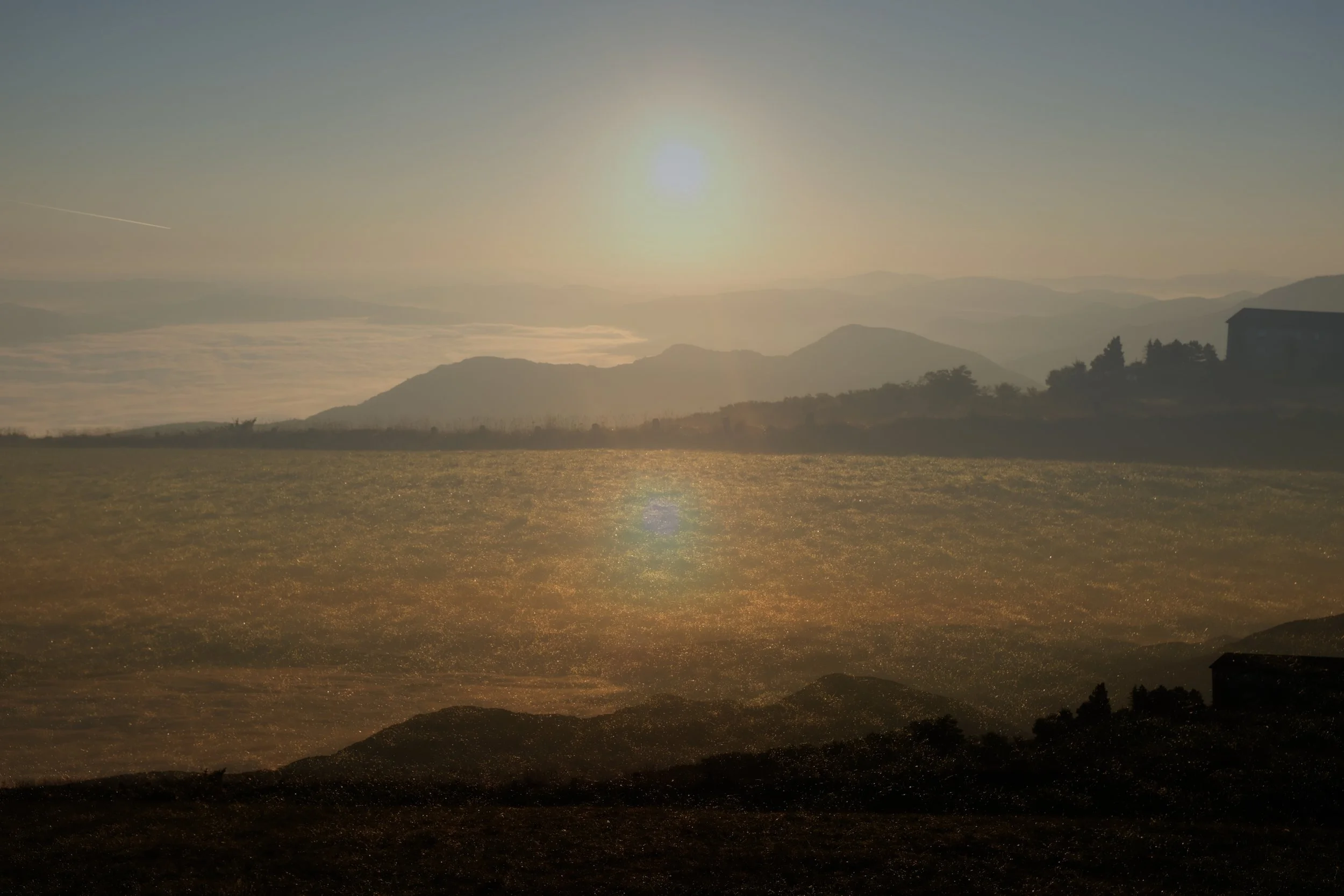 Paesaggio montano con il sole al tramonto, con nuvole e una luce calda