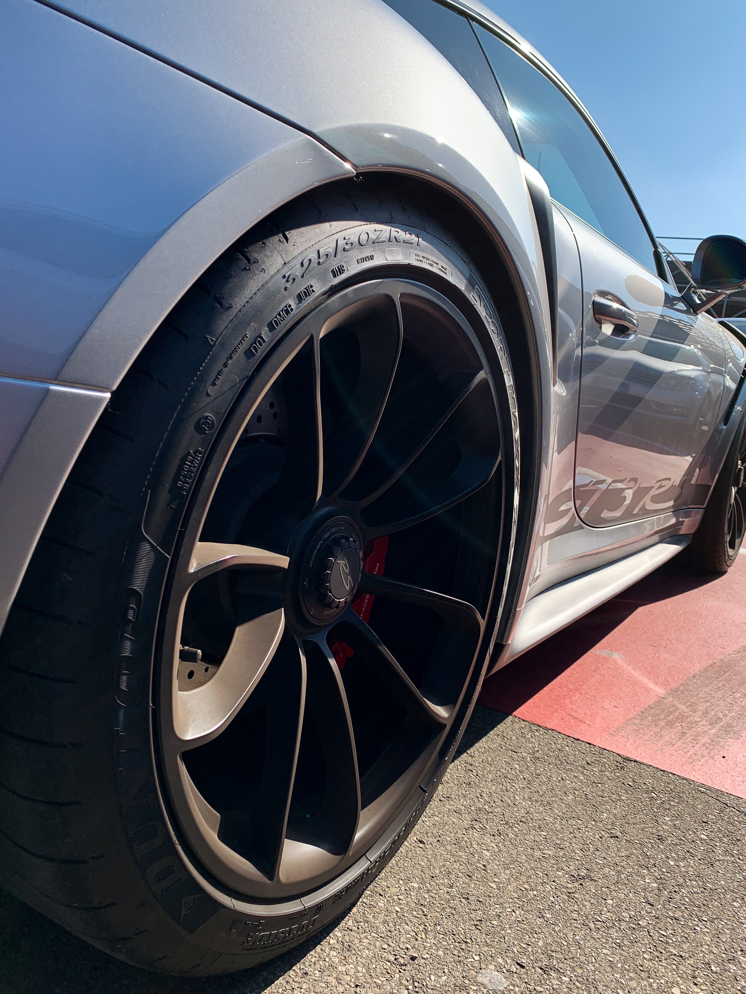 Particolare di un'auto sportiva di colore grigio con cerchi neri e dettagli in argento, fotografata da vicino sotto il sole.