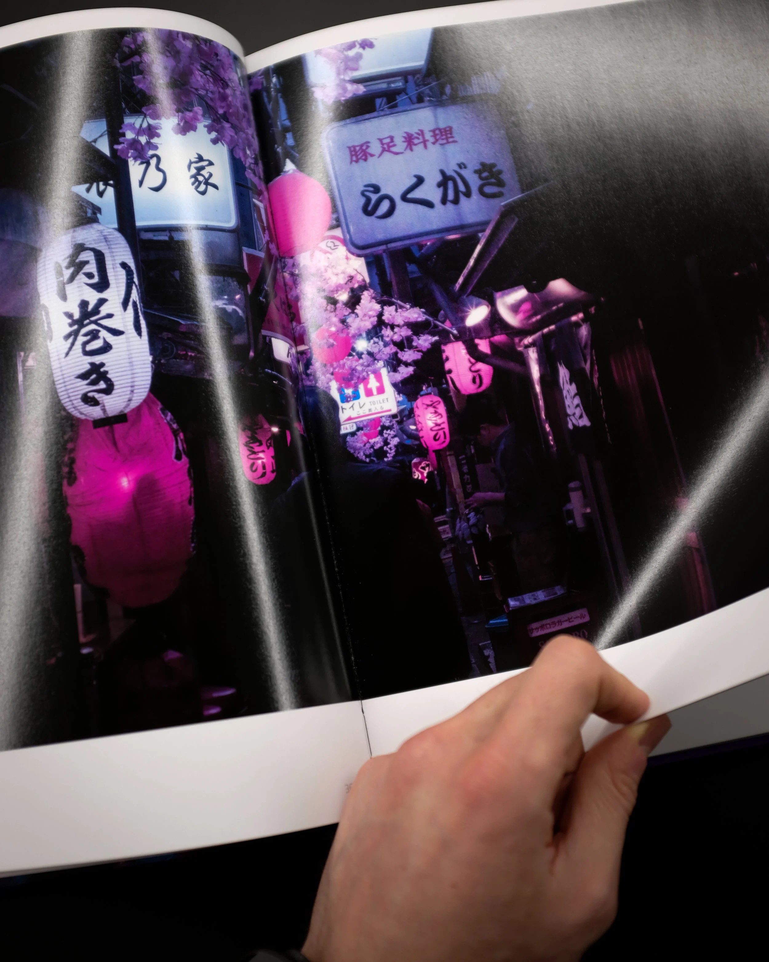 Foto di un negozio di strada con insegne in giapponese, lanterne rosa e fiori di ciliegio finti lungo la strada, ambiente urbano vivo.