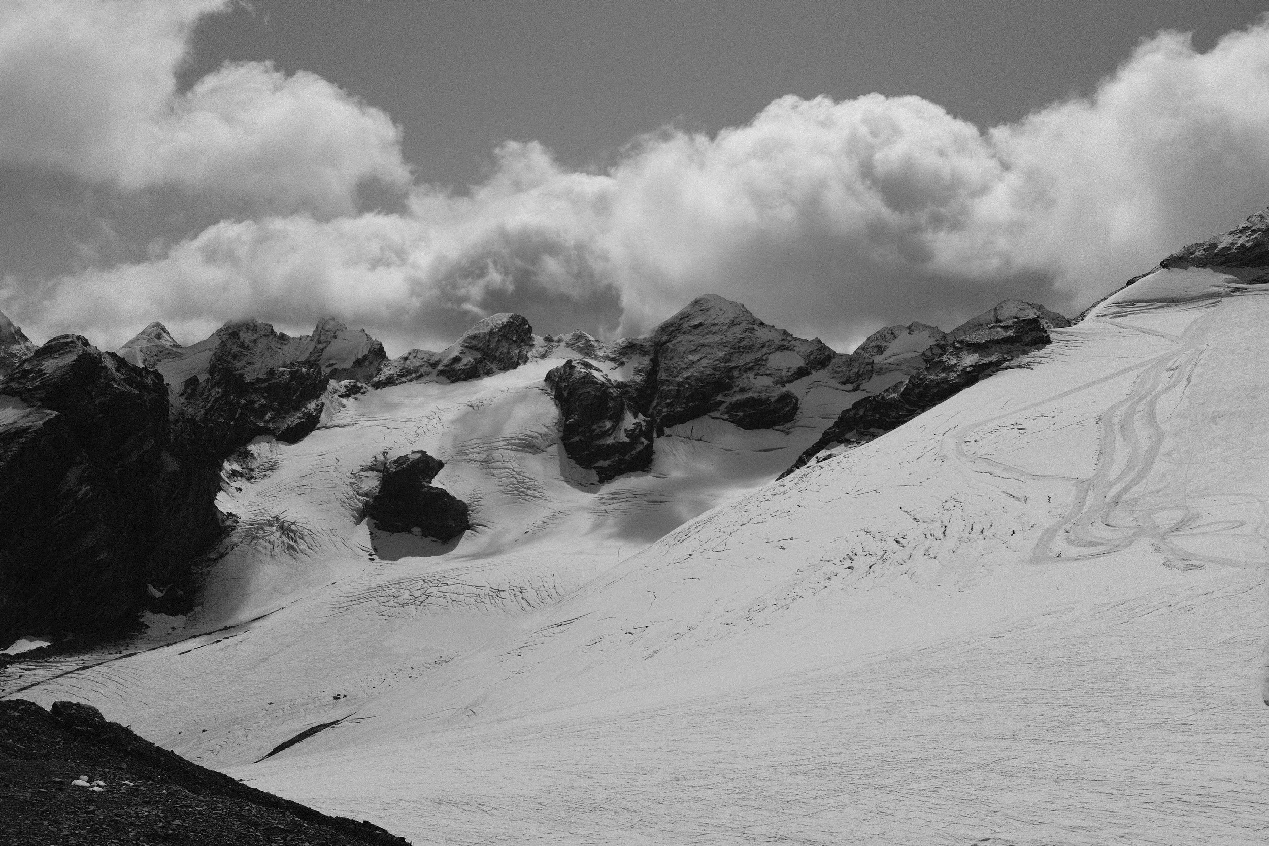 Montagne innevate con nuvole sopra, in bianco e nero.