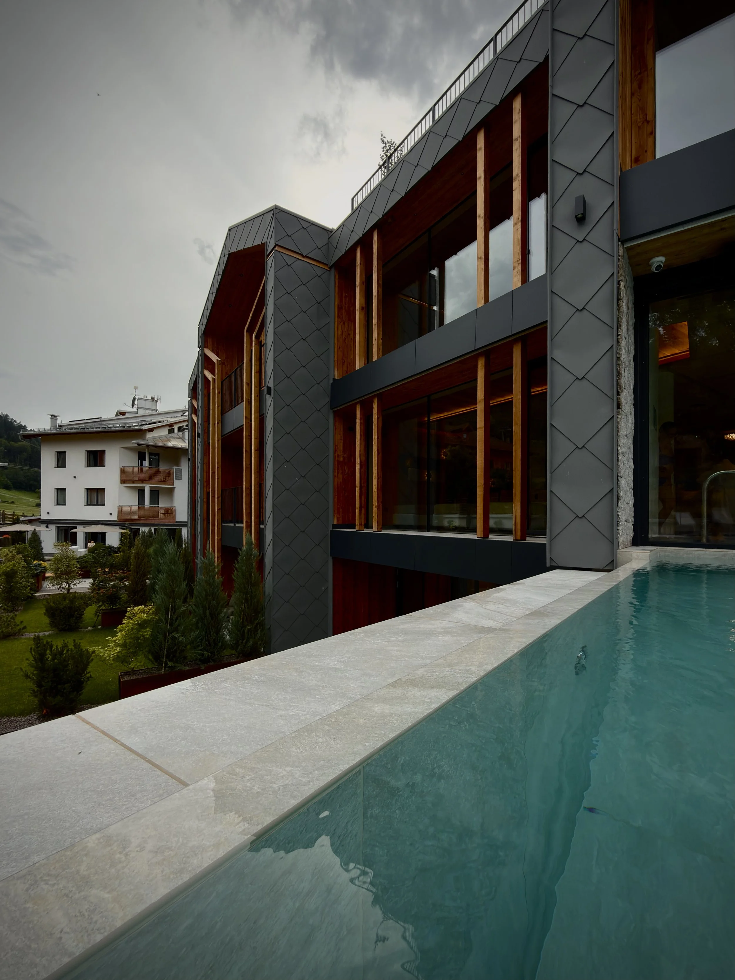 Edificio moderno con facciata in metallo e legno, piscina e giardino sottostante