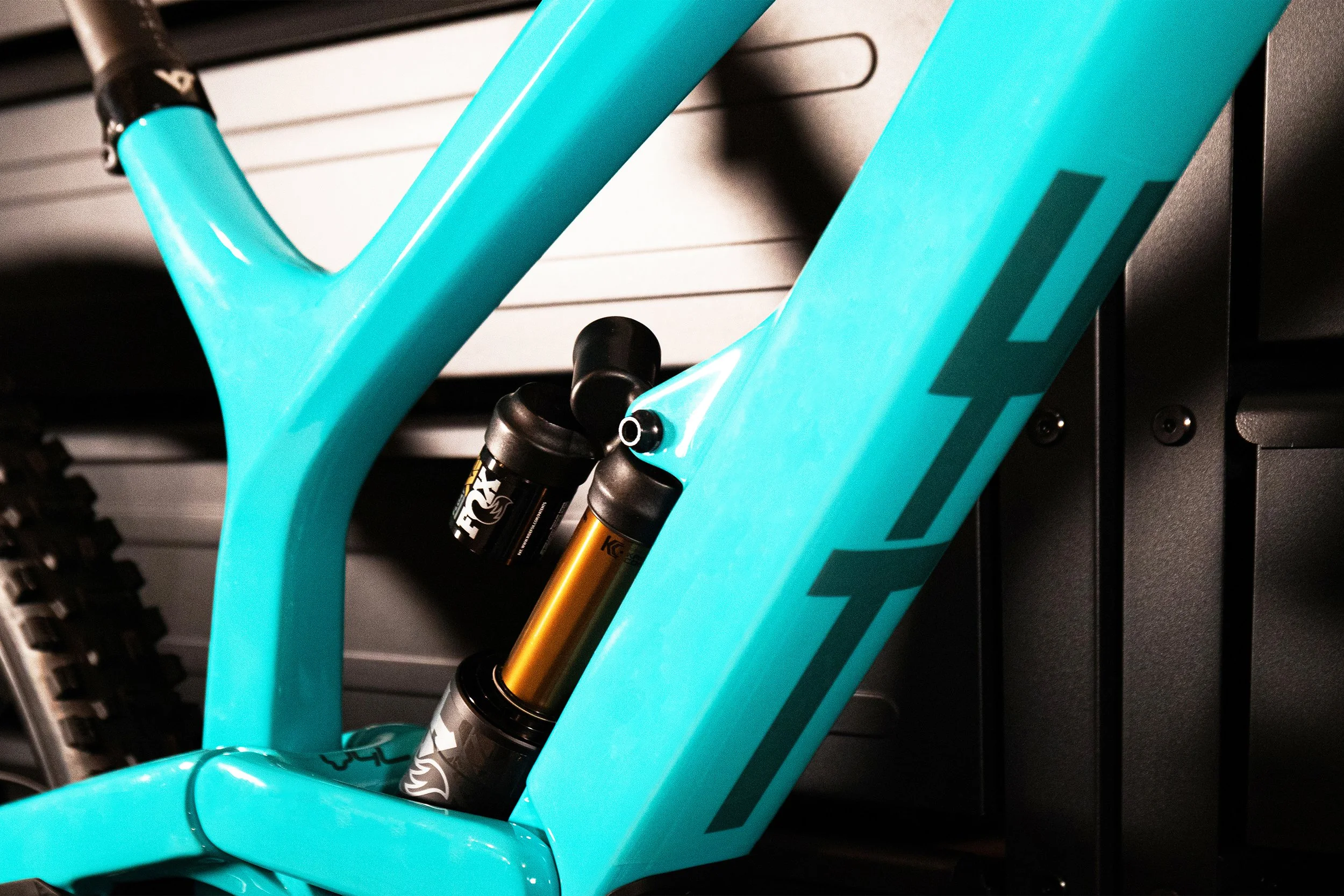 Particolare di una bicicletta con telaio azzurro e sospensioni anteriori dorate, montata su un supporto.