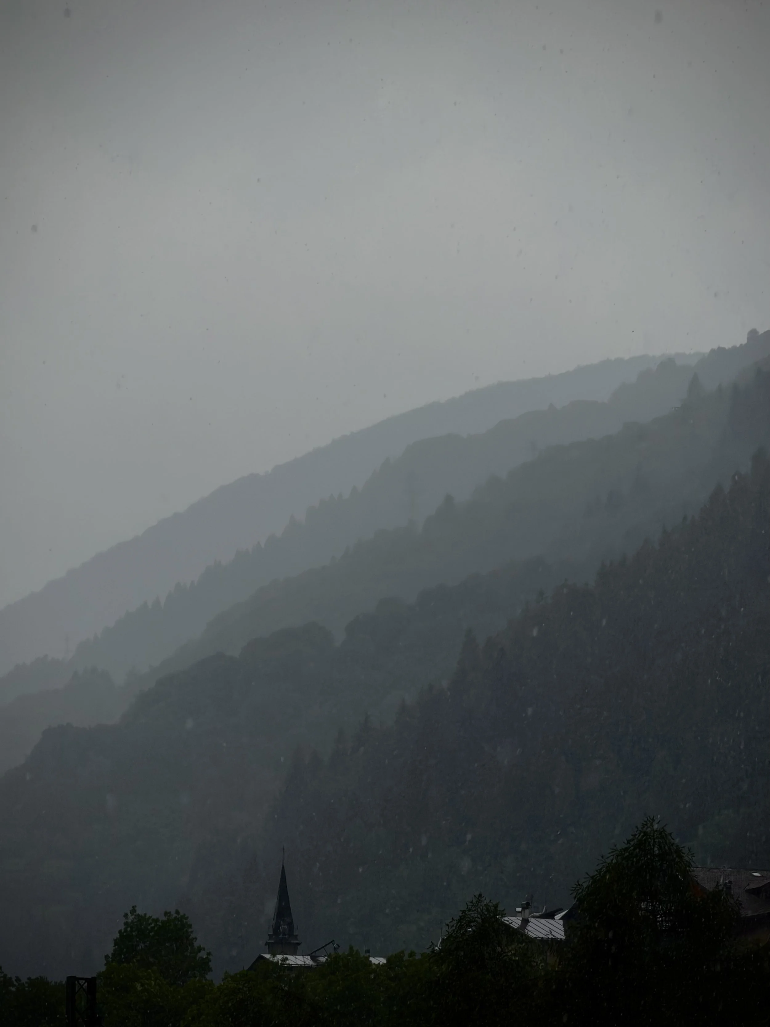 Paesaggio montano con nuvole basse e un villaggio con chiese e case in primo piano.