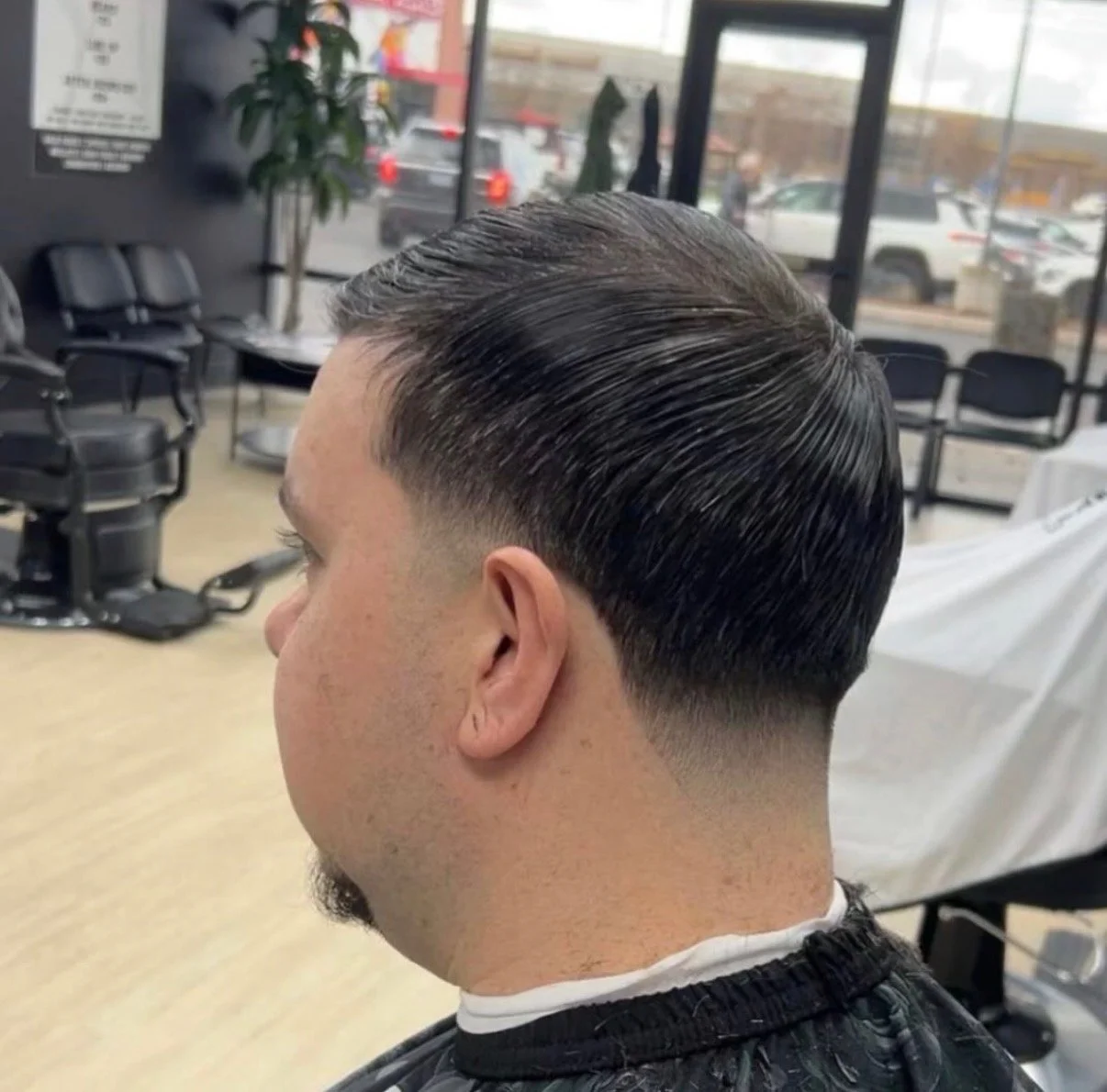 Man with slicked-back, short haircut and faded sides sitting in a barber shop.