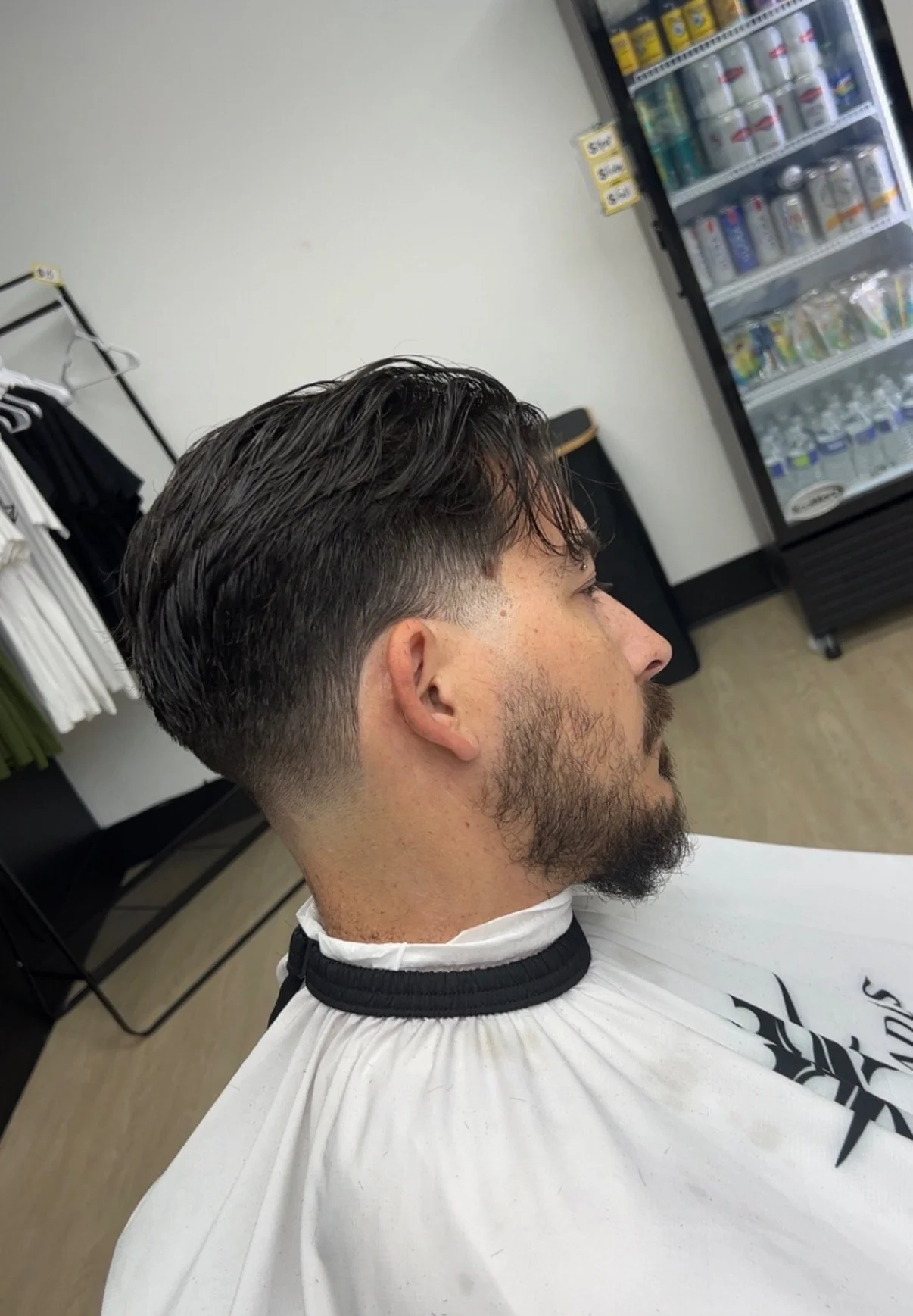 Man with a fresh haircut and beard sitting in a barber's chair in a barbershop.