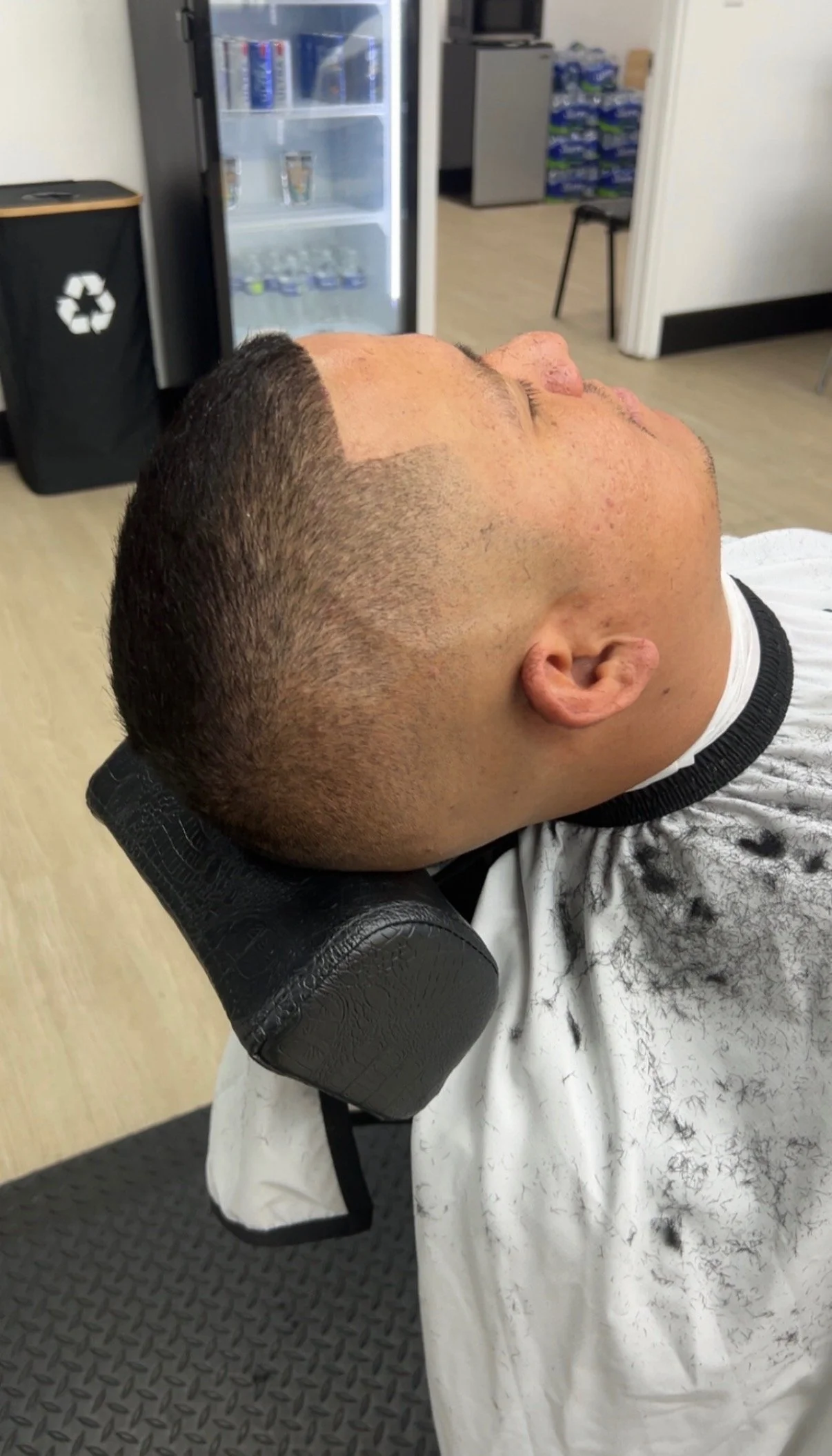 A man with a fresh haircut lying back in a barber's chair in a barbershop or salon.
