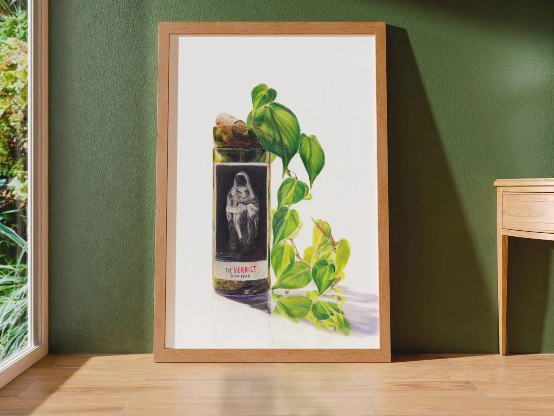 A framed hyper-realistic coloured pencil illustration leaning against a green wall. Depicting a wine bottle with a label reading "The Verdict" and a plant with green, leafy vines growing beside it.