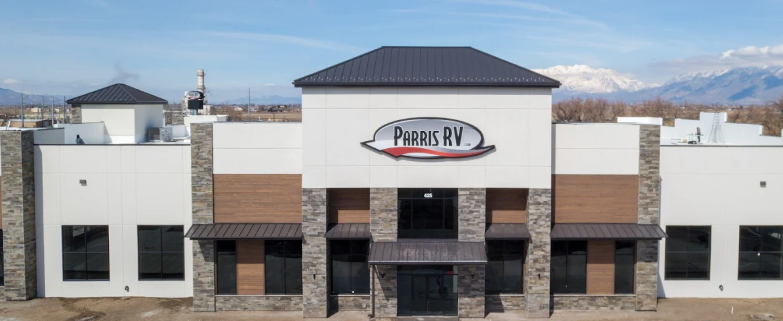 Exterior view of Parris RV building with white walls, stone accents, and a sign on top, located in a semi-urban area with mountains in the background.