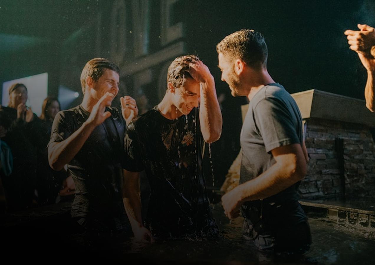Three men being baptized in a church, with two in water and one celebrating.