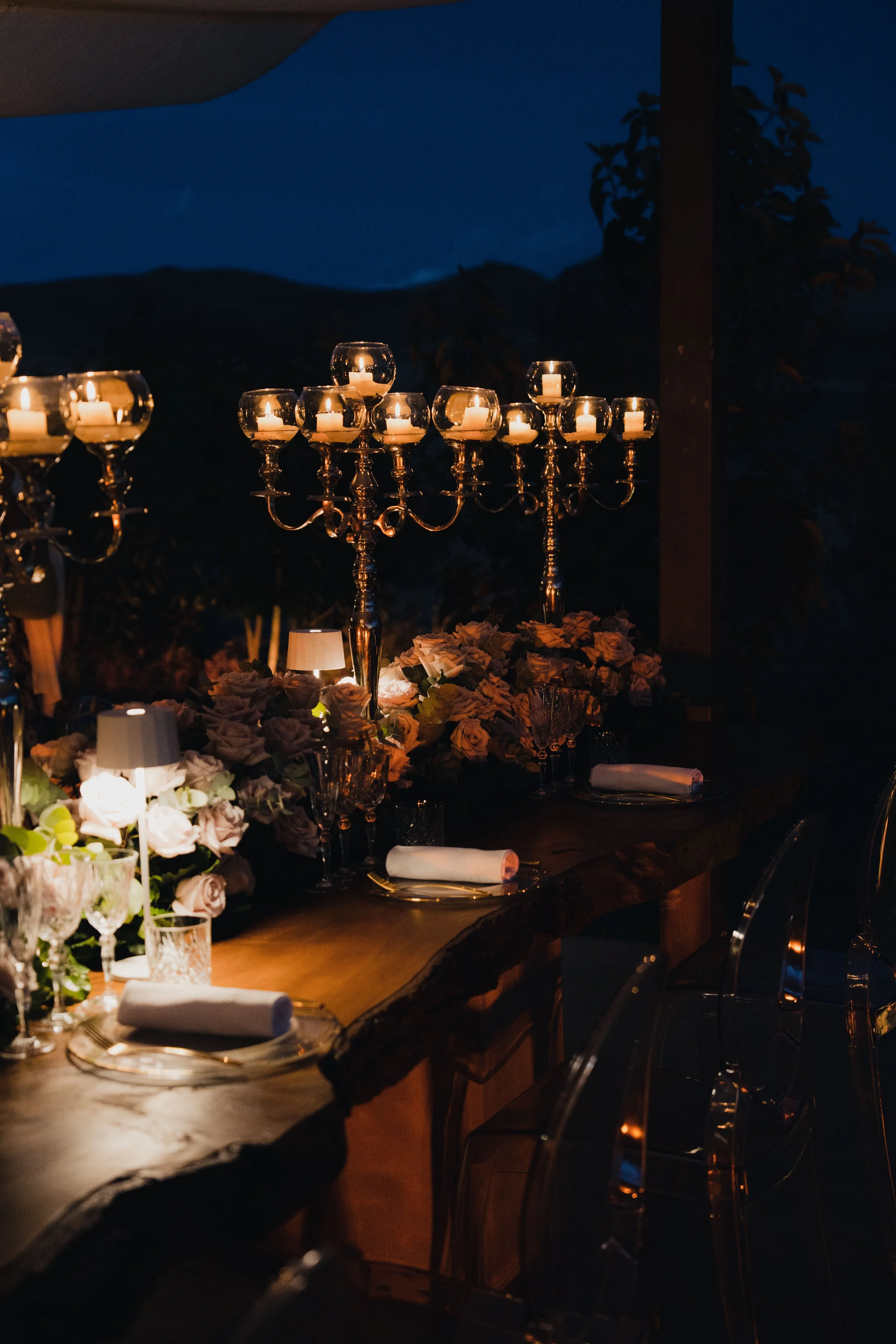 A candlelit dinner table decorated with floral arrangements, candelabras, and table settings at night.